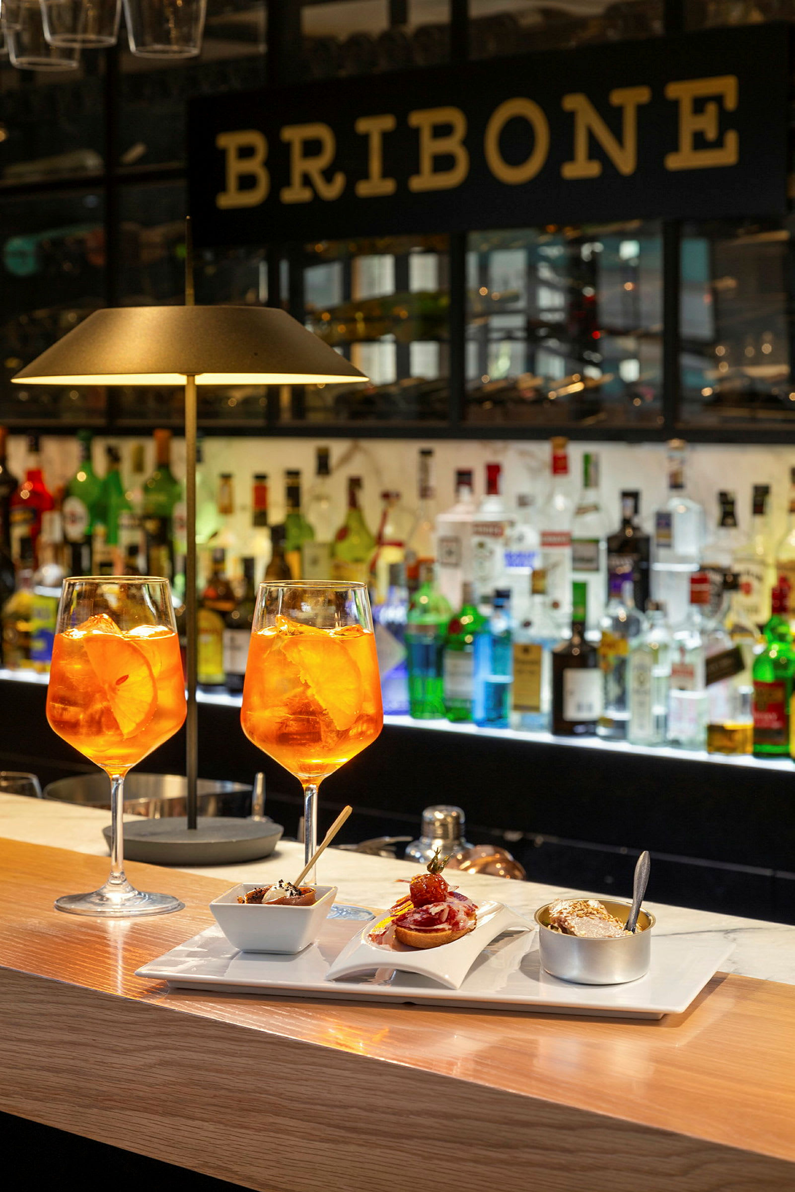 To glas med orange drik og en tallerken med forskellige småretter står på en bardisk. (AI-genereret tekst)