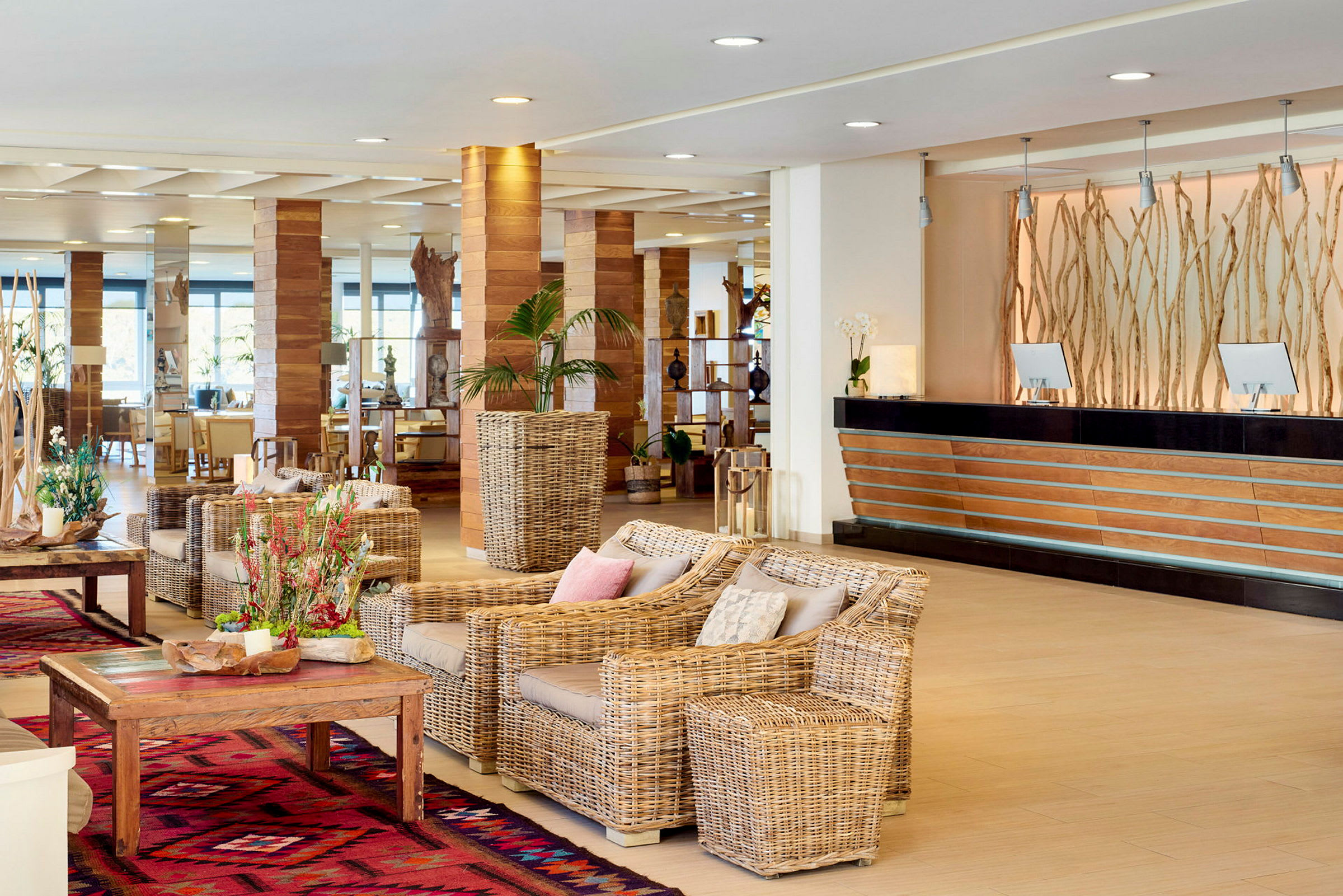 Lyst og åbent hotellobbyområde med siddegruppe af rattanmøbler og receptionsdisk i træ og sort. (AI-genereret tekst)