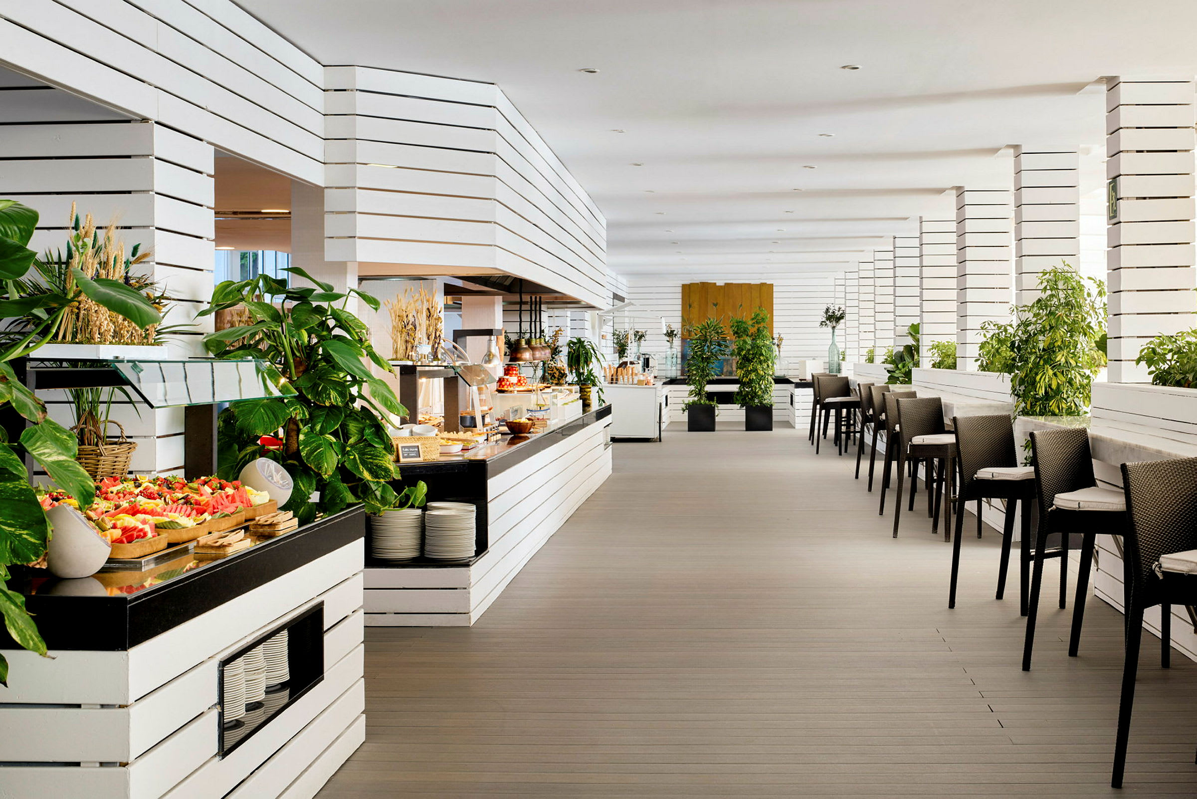 Indretning af en moderne restaurant med hvide træpaneler, grønne planter og serveringsborde fyldt med mad. (AI-genereret tekst)