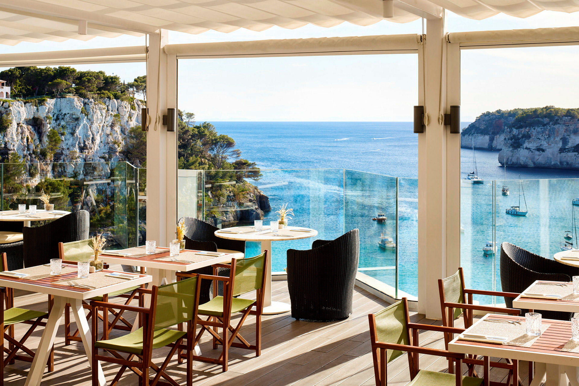 En restaurantterrasse med borde og stole, med udsigt over havet og klipper. (AI-genereret tekst)