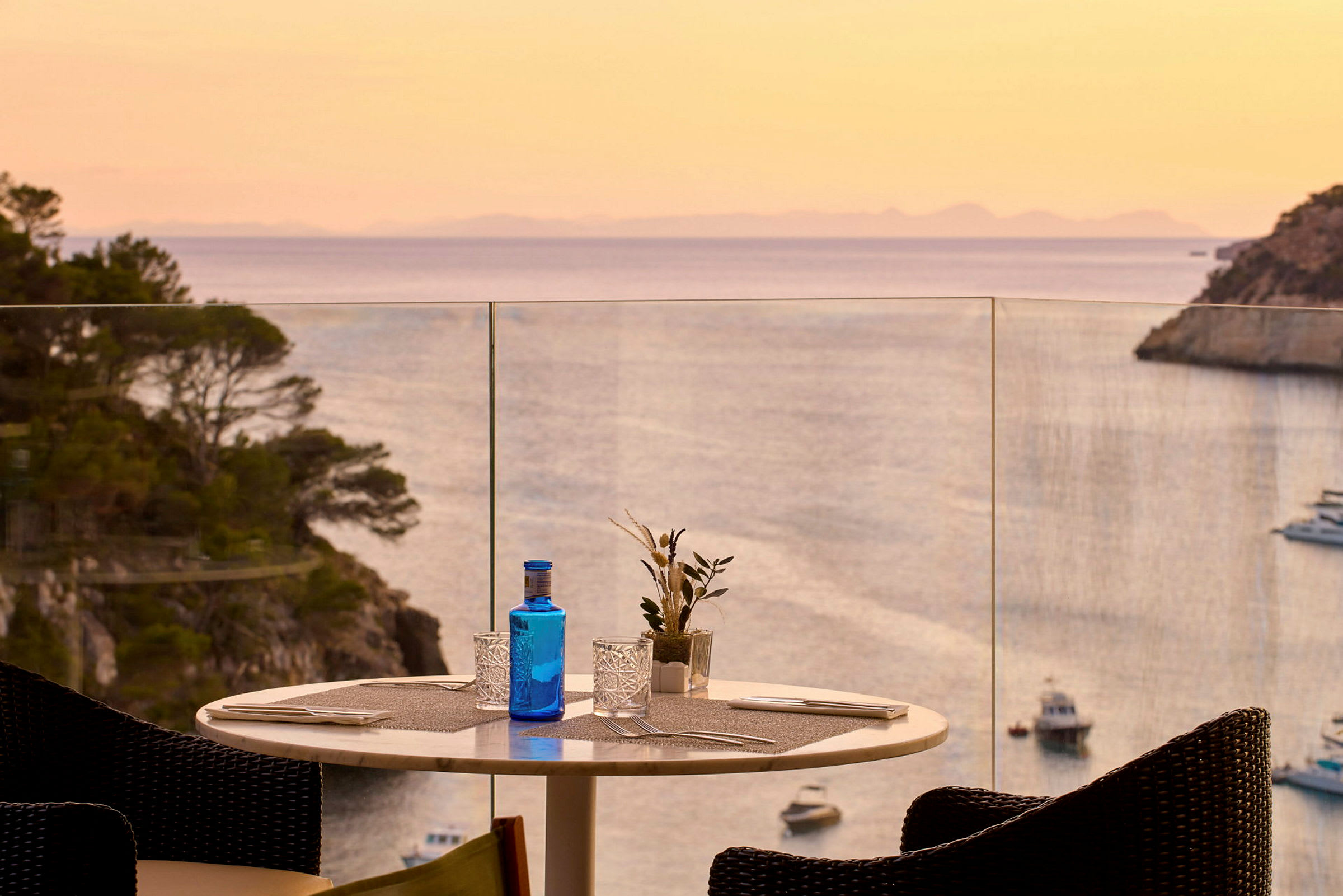 Et dækket bord på en terrasse med udsigt over havet og en solnedgang. (AI-genereret tekst)