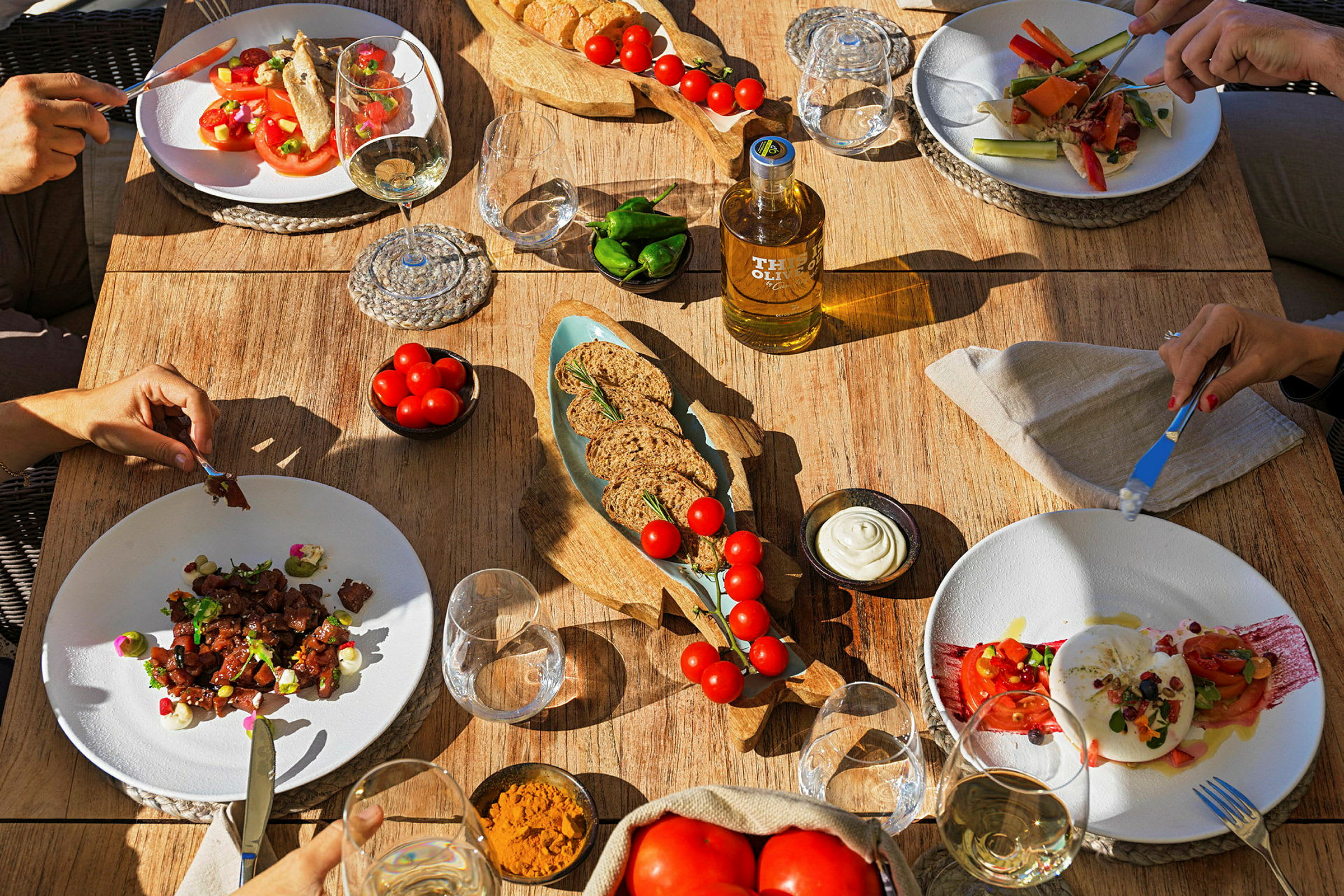 Et spisebord med tallerkener fyldt med salat og andre retter, omgivet af glas og skåle med olie, brød og tilbehør. (AI-genereret tekst)