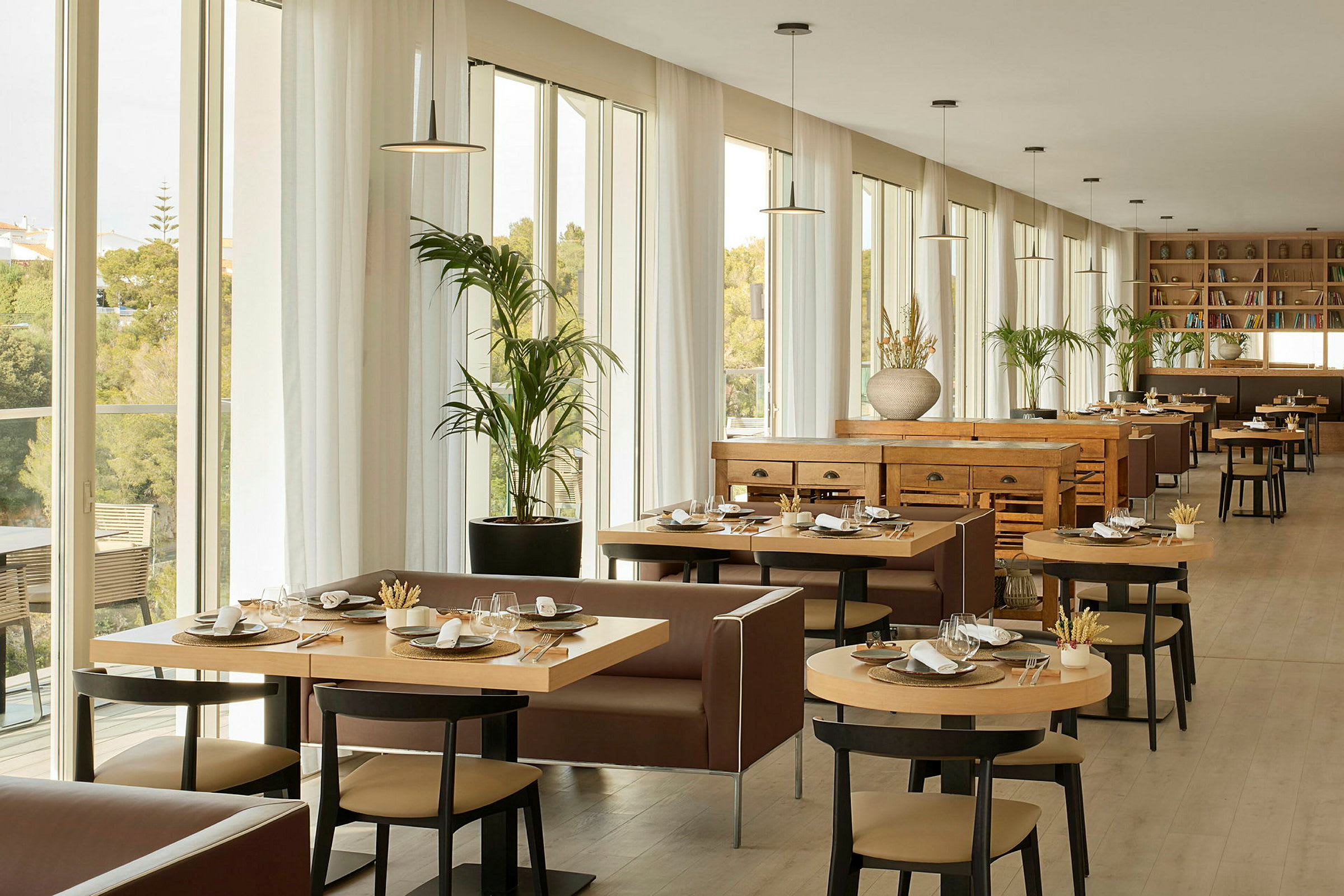 En lys og rummelig restaurant med store vinduer, moderne møbler og borde dækket til måltider. (AI-genereret tekst)