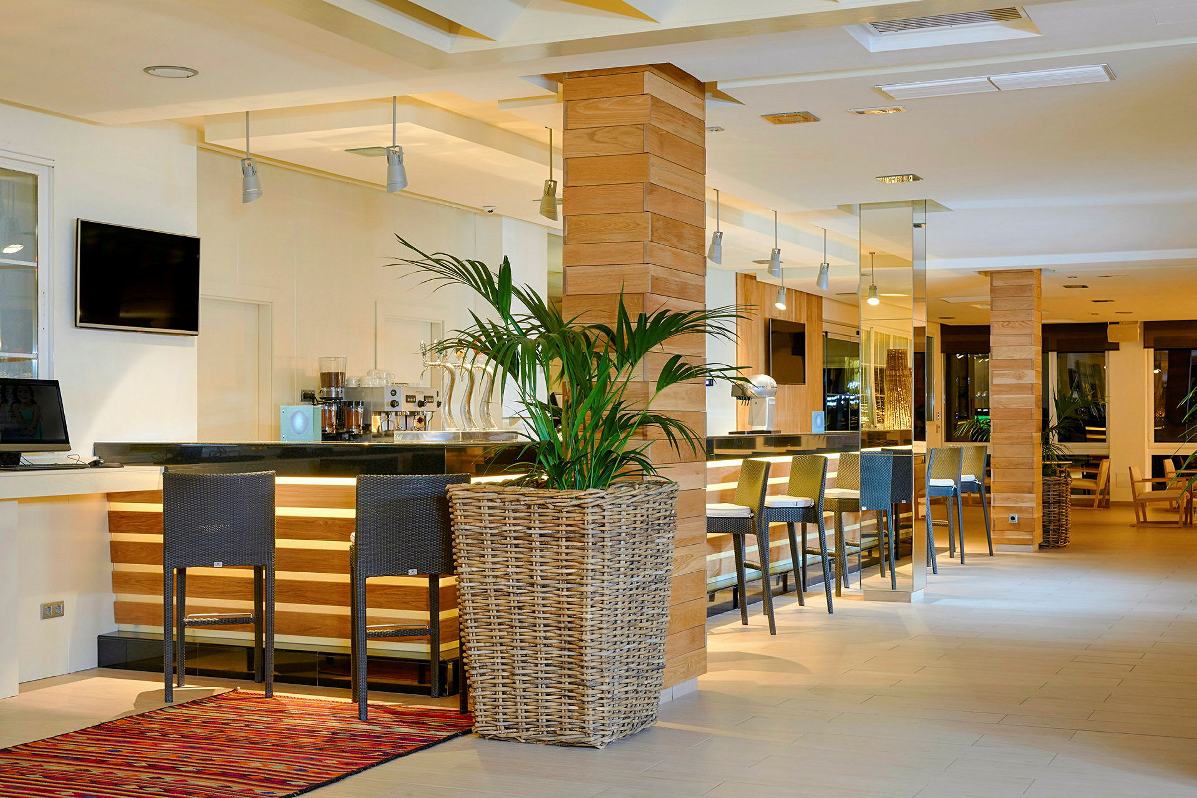 Billede af en moderne og stilfuld hotelbar med høje stole, en bardisk i sort, træpaneler og en stor urtepotteplante i forgrunden. (AI-genereret tekst)