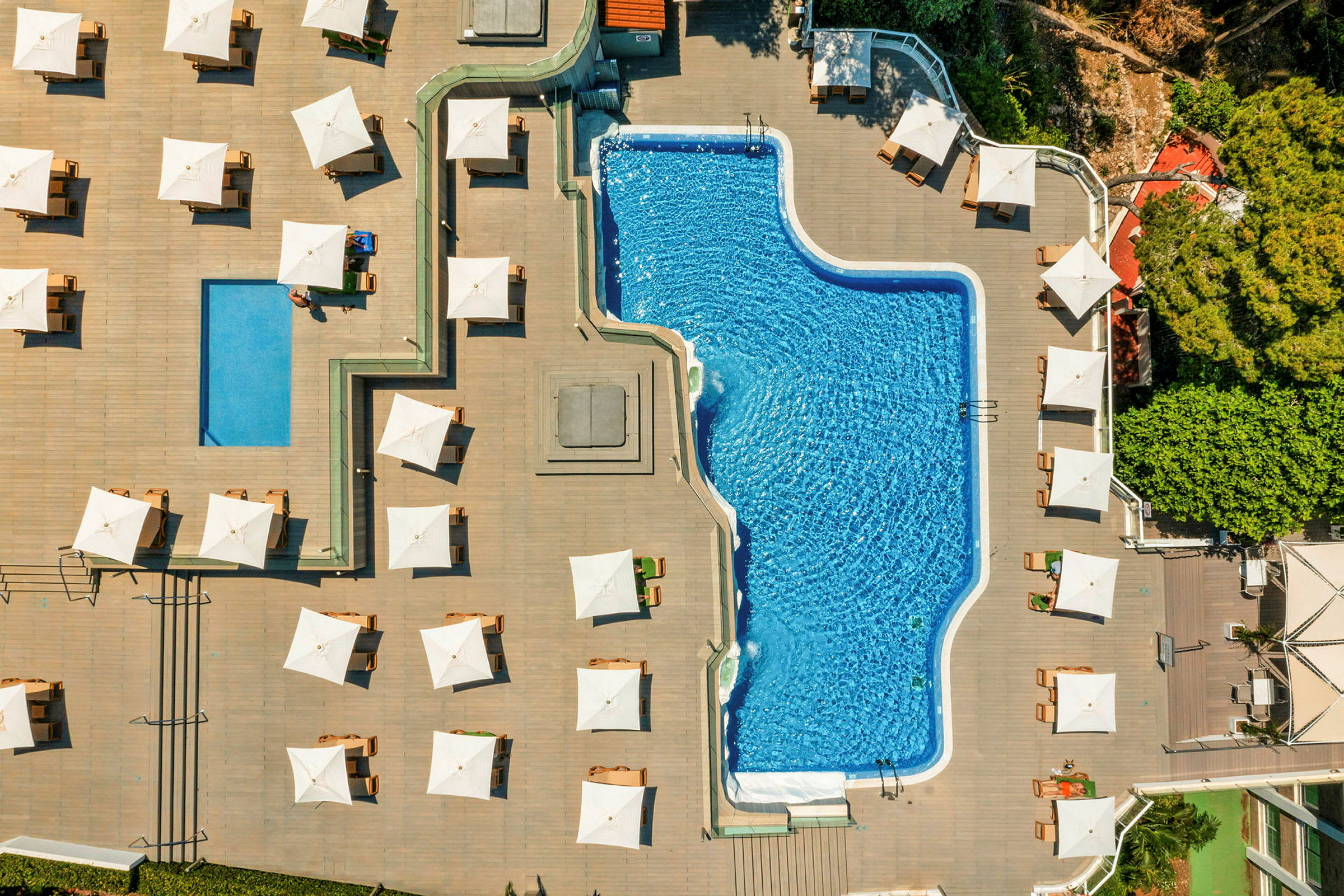 Luftfoto af en pool omgivet af løbebaner og liggestole med hvide parasoller. (AI-genereret tekst)