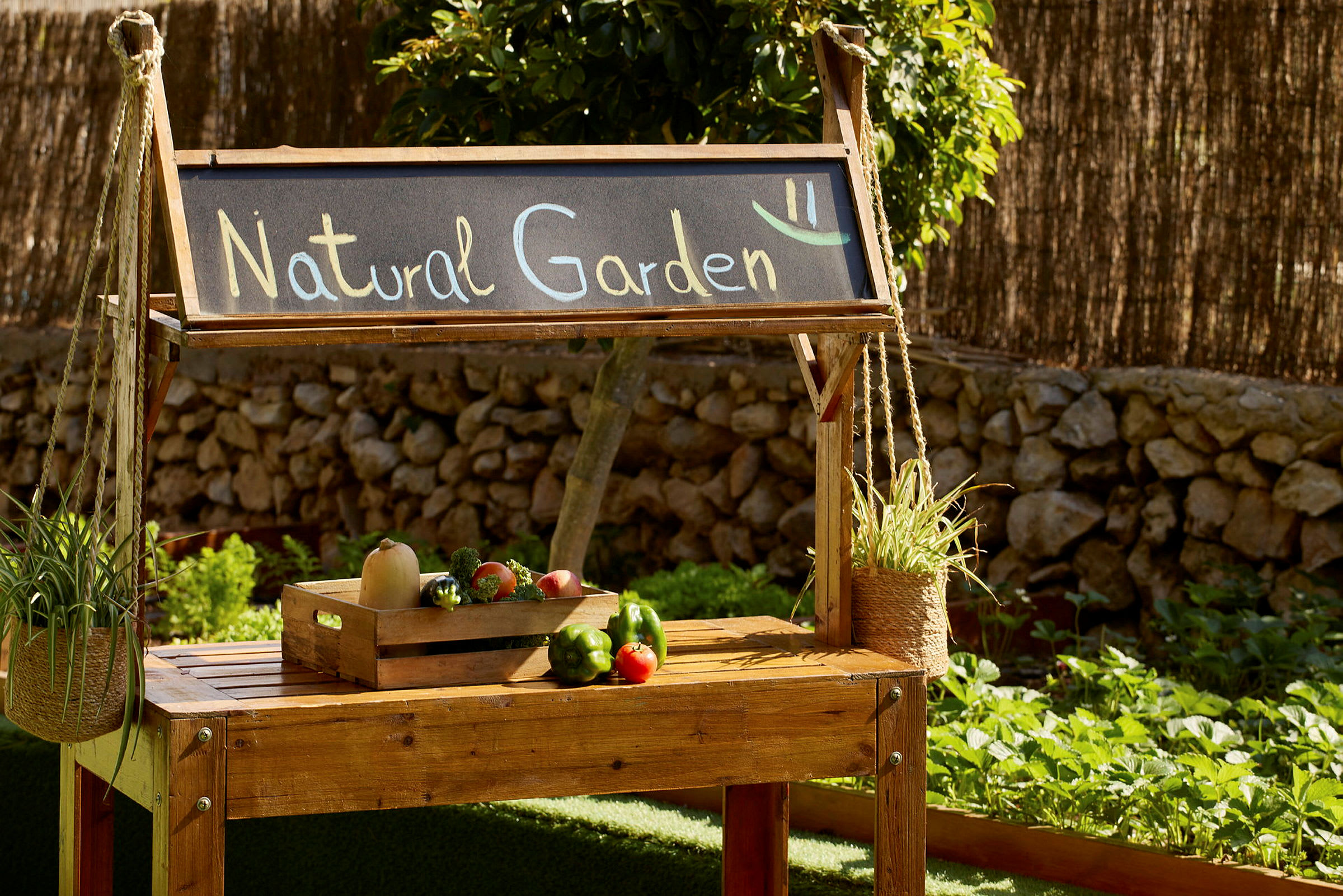 Trævogn med skiltet "Natural Garden" og en kasse med grøntsager, omgivet af have og planter. (AI-genereret tekst)