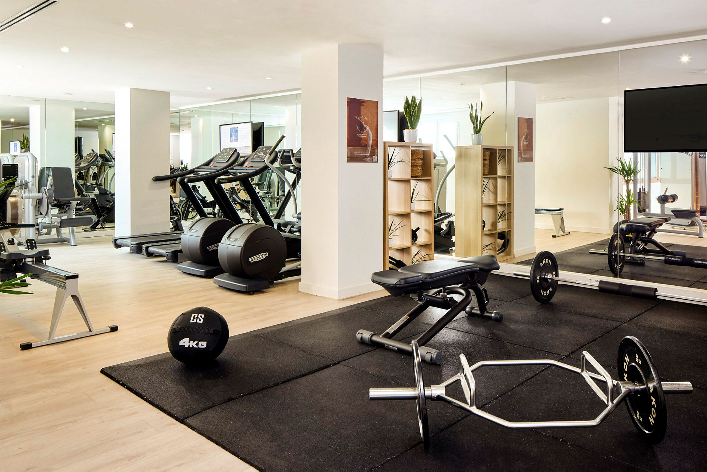 Et træningsrum med forskellige fitnessmaskiner, frie vægte og planter i et lyst område. (AI-genereret tekst)
