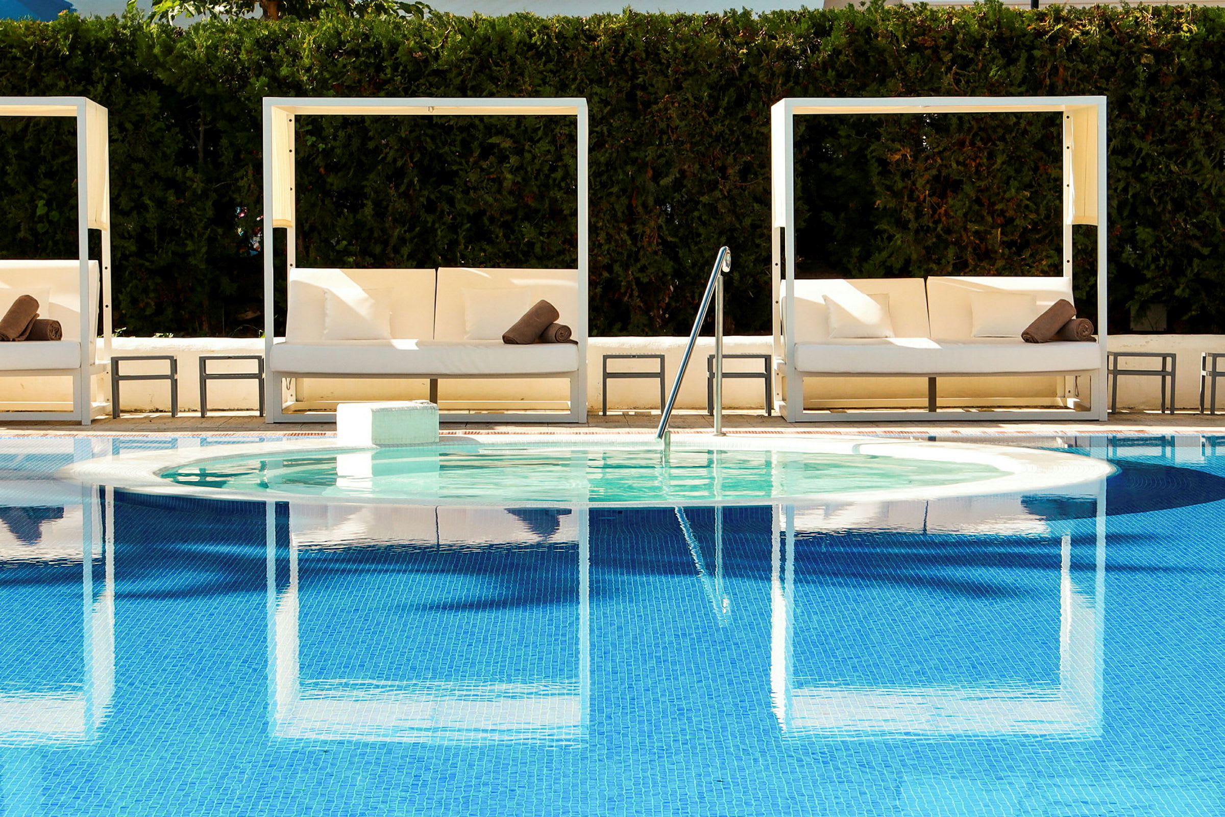Udendørsmøbler og glasstole ved en pool med spejlblåt vand. (AI-genereret tekst)