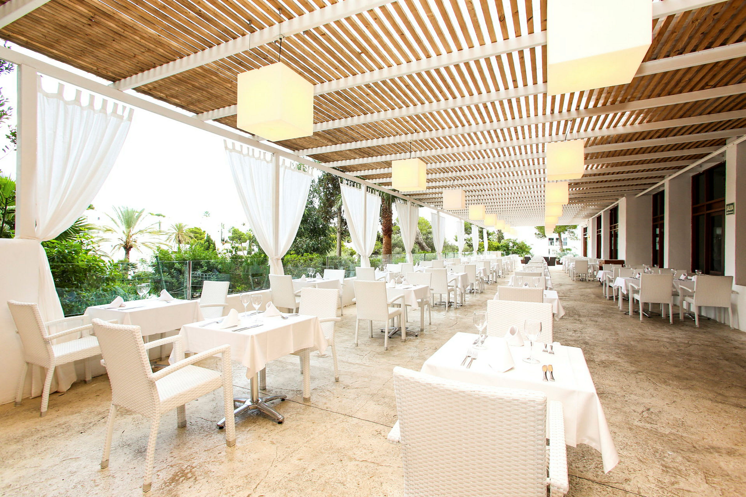 Restaurant med hvide borde og stole under tag nær grønne områder. (AI-genereret tekst)