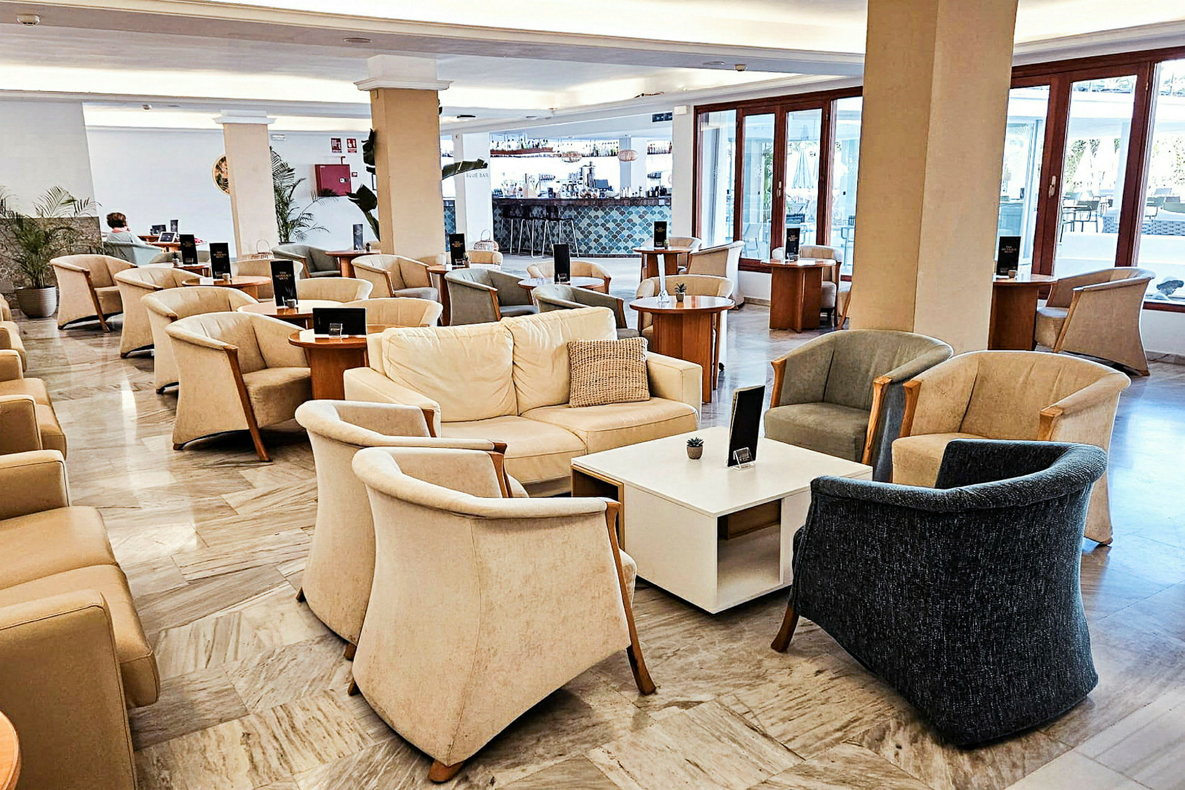 En lounge med komfortable lænestole, sofaer og borde, med store vinduer i baggrunden. (AI-genereret tekst)
