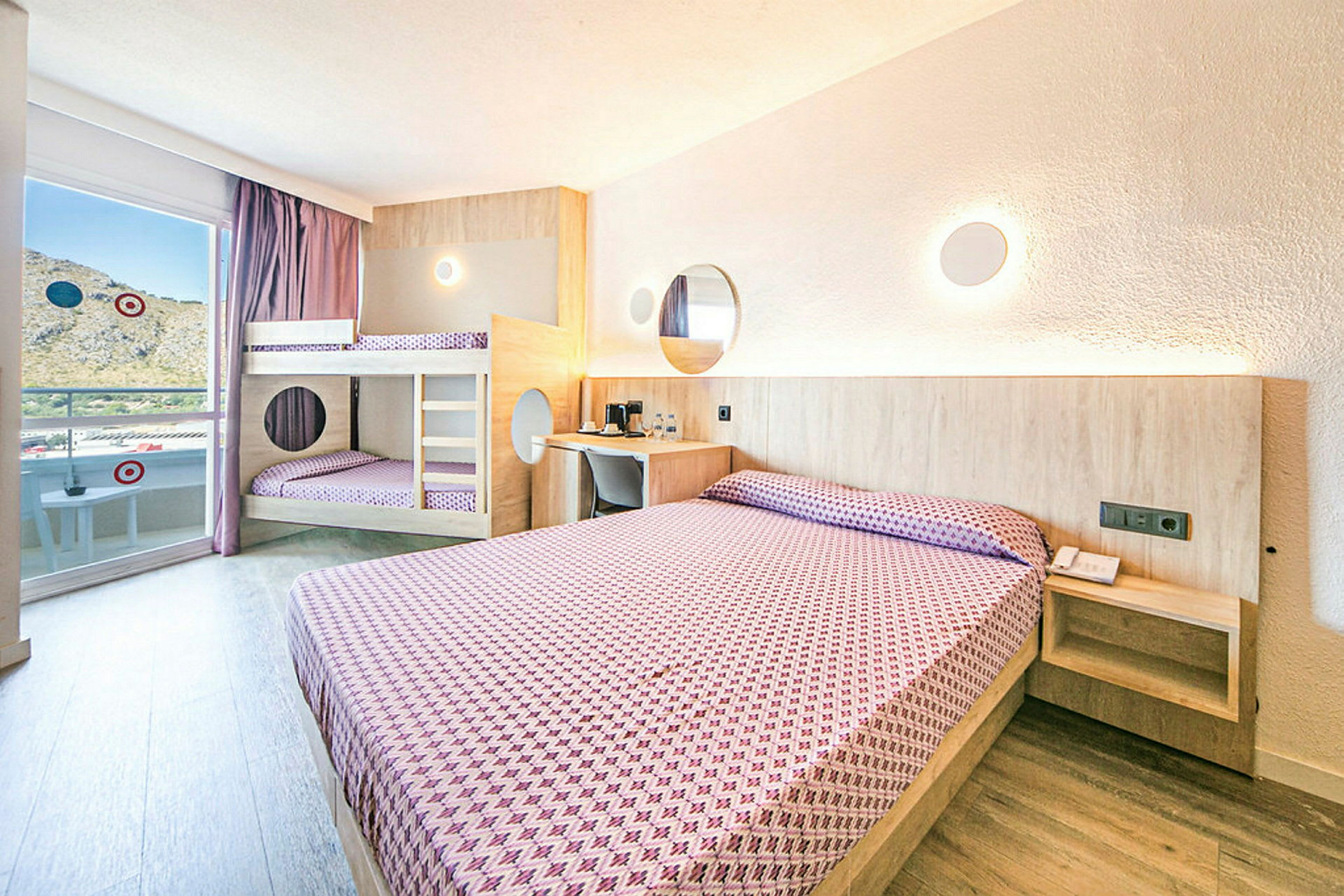 Et hotelværelse med en dobbeltseng og en køjeseng, begge opredte med lilla mønstrede sengelinned, lyse vægge og trædetaljer. (AI-genereret tekst)