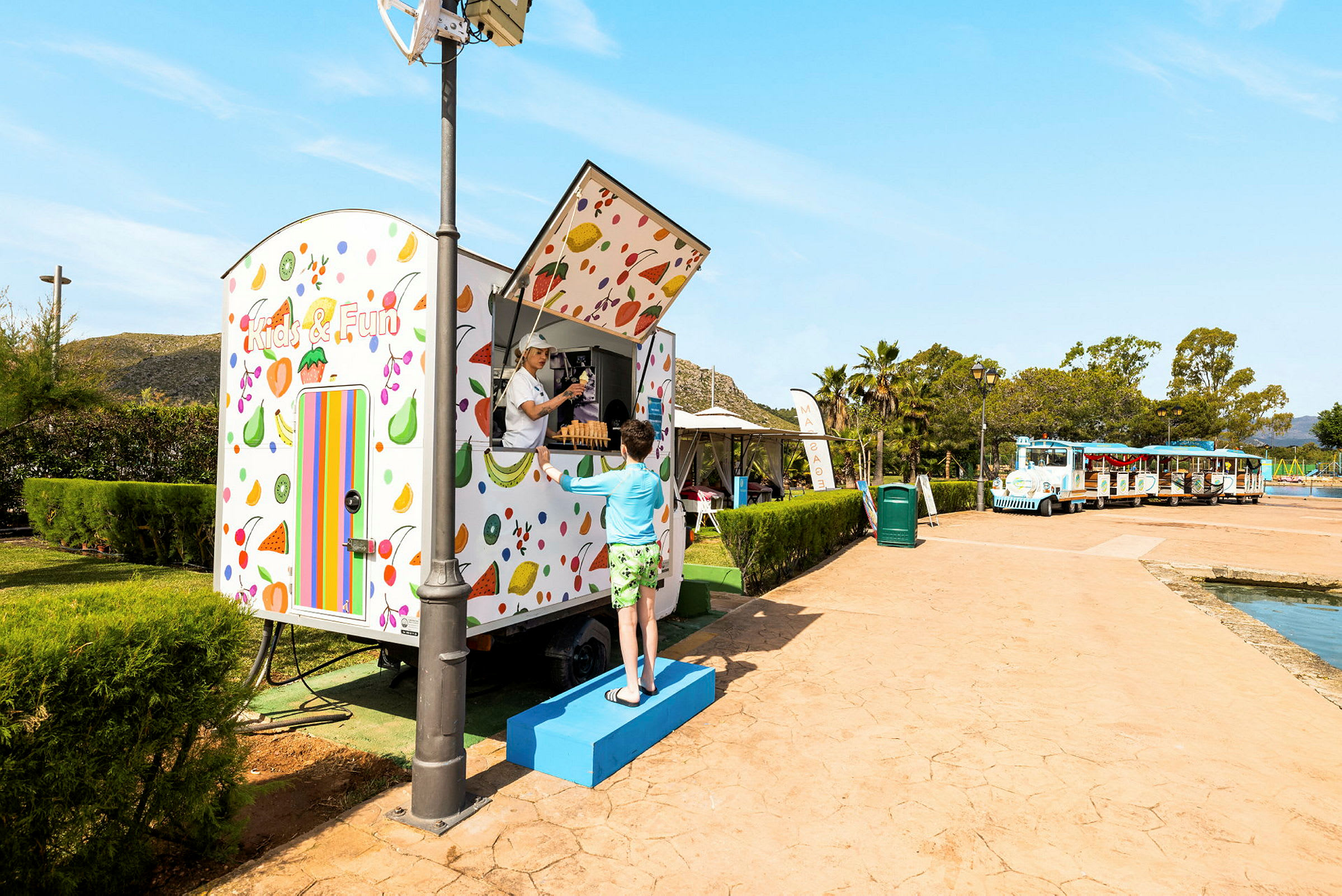 En farverig kiosk med teksten "Kids & Fun". En person står foran og taler med personalet i kiosken. (AI-genereret tekst)