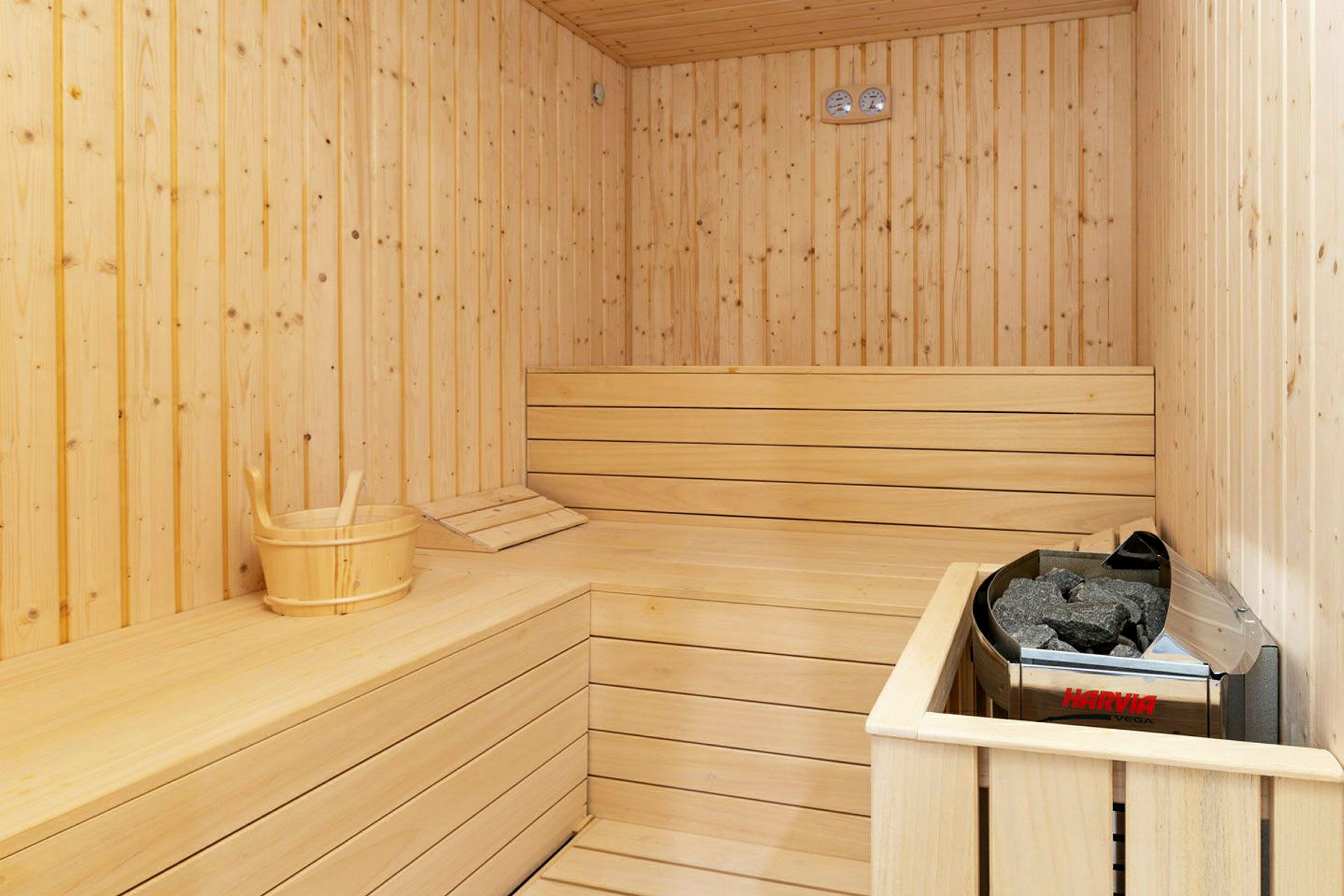En sauna med træpaneler, en sauna bænk og en spand ved siden af en saunaovn. (AI-genereret tekst)