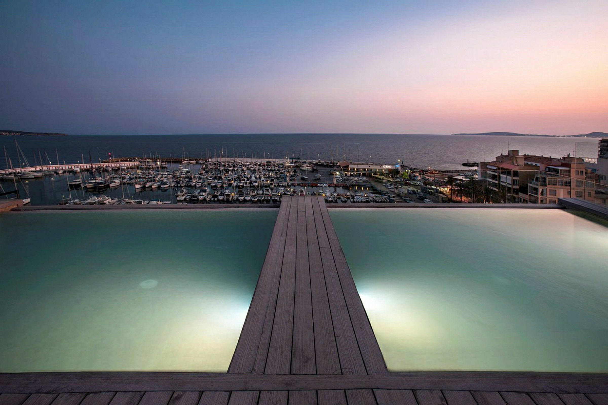En infinitypool med udsigt over en marina og havet ved solnedgang. (AI-genereret tekst)