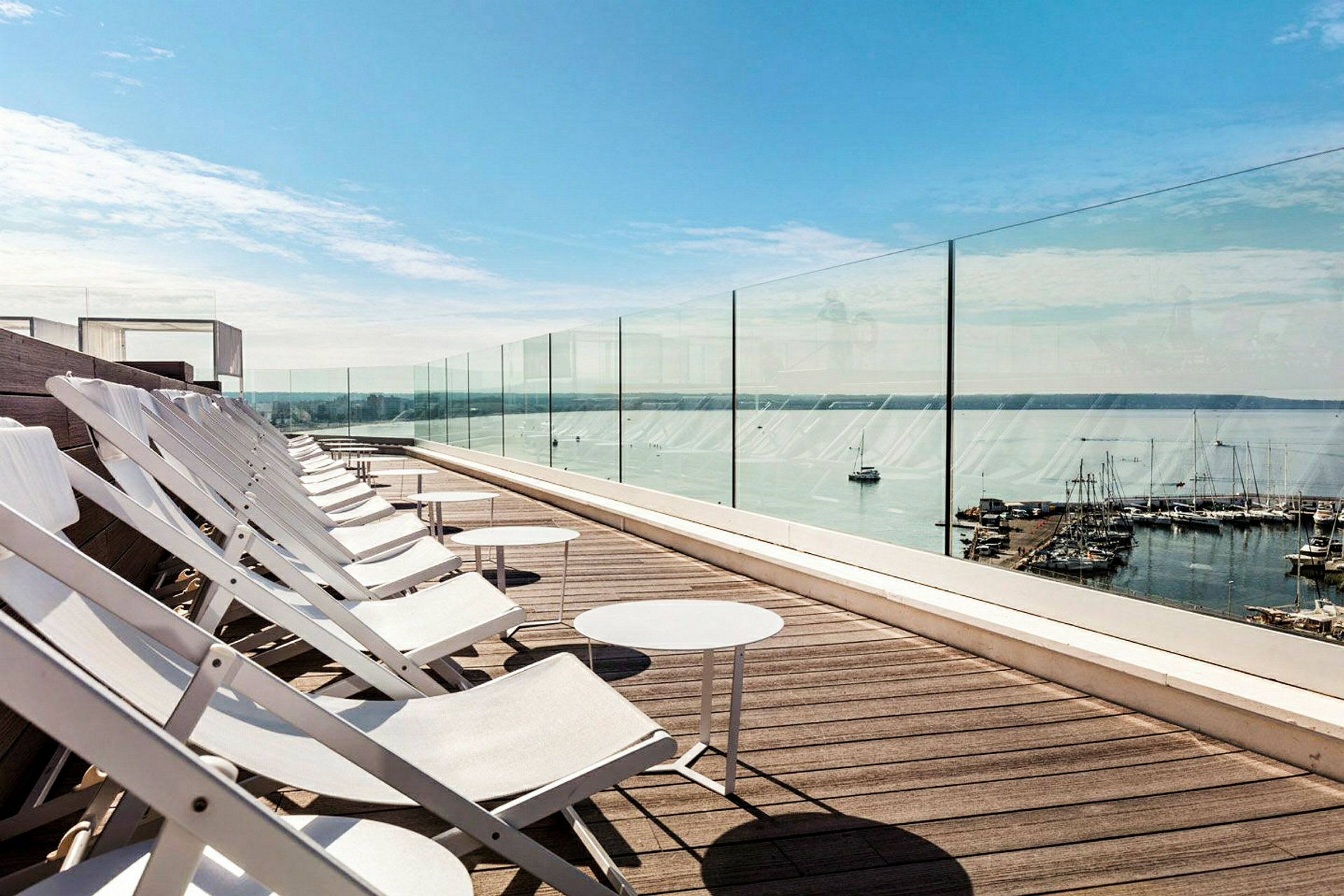 Liggestole på en tagterrasse med udsigt over havet og en lystbådehavn. (AI-genereret tekst)