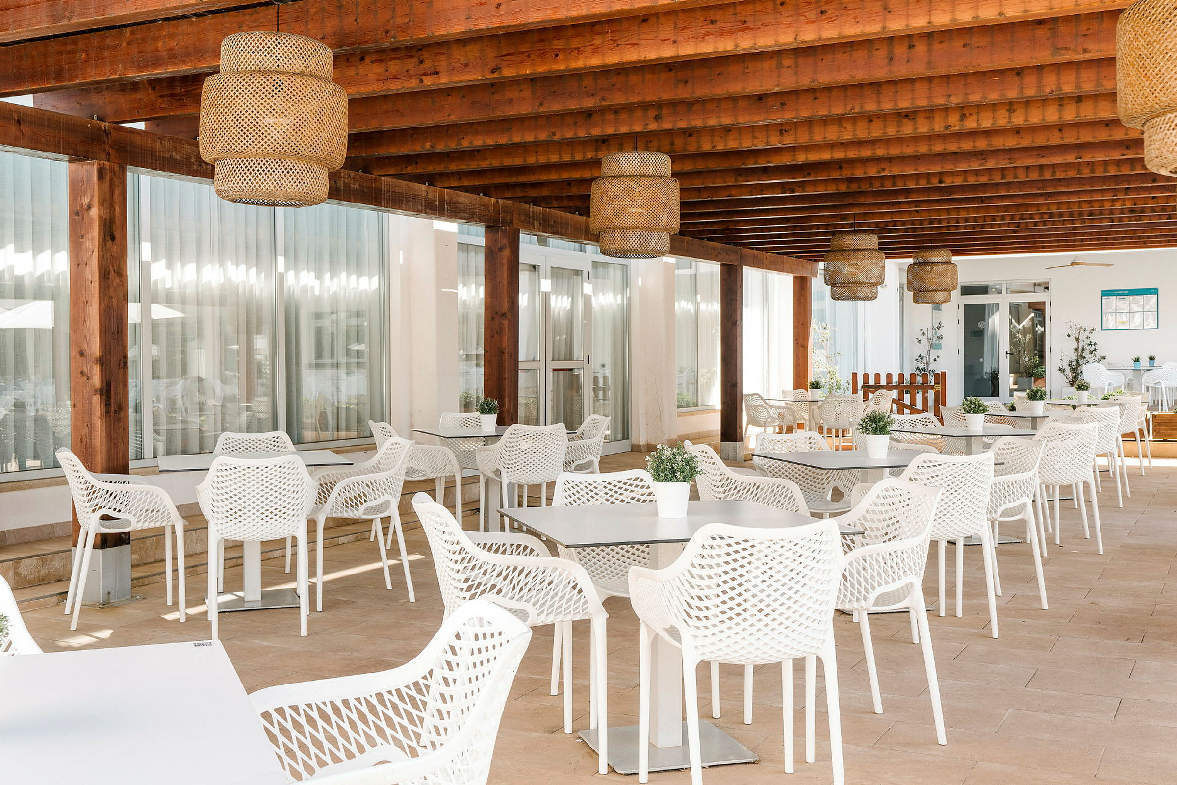 Billede af en terrasse med loft af træbjælker, hvide borde og stole med netmønster samt potteplanter som dekoration. (AI-genereret tekst)
