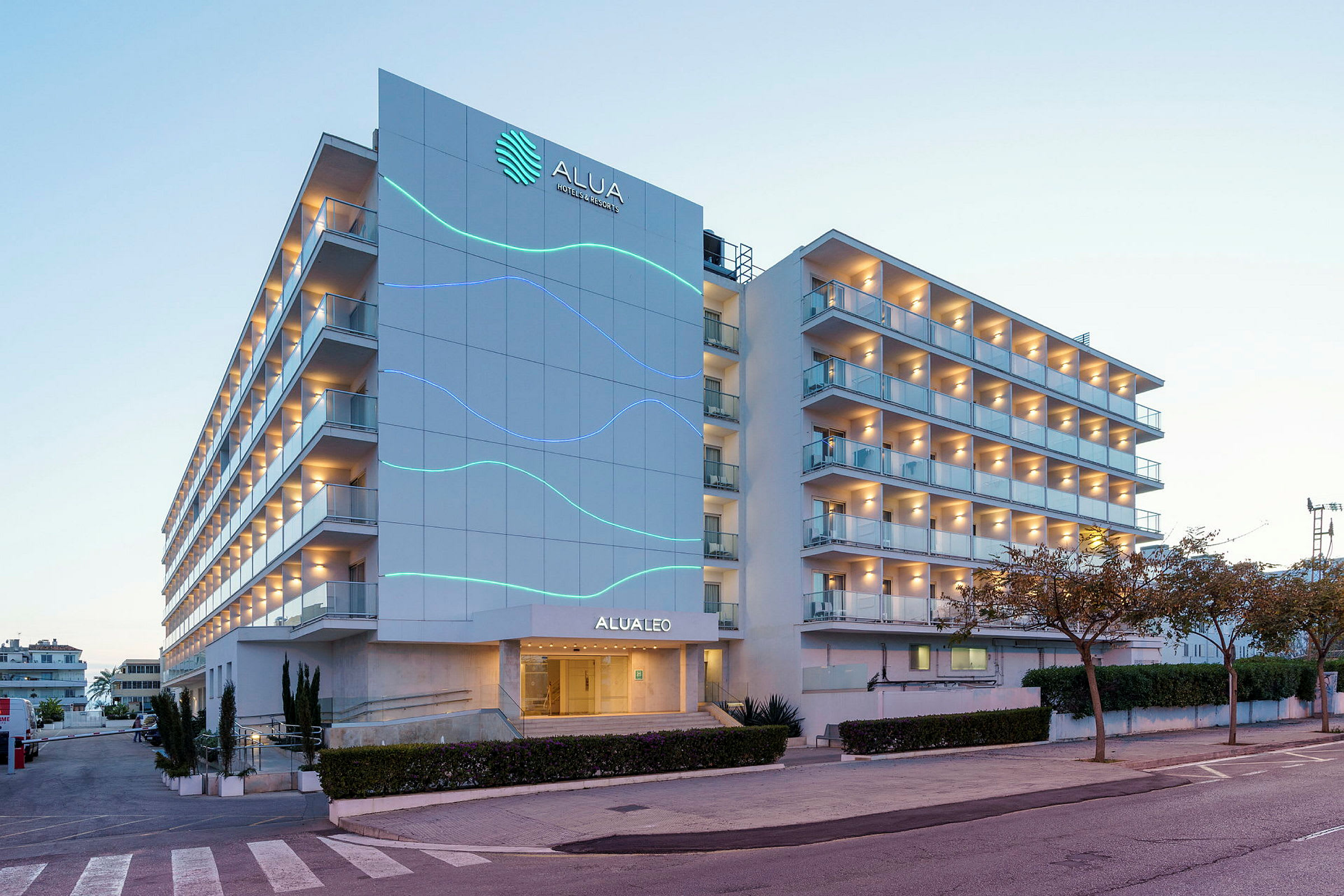 Et fleretasjes hotel med altaner og facadeudsmykning, beliggende ved en vej og omgivet af træer. (AI-genereret tekst)