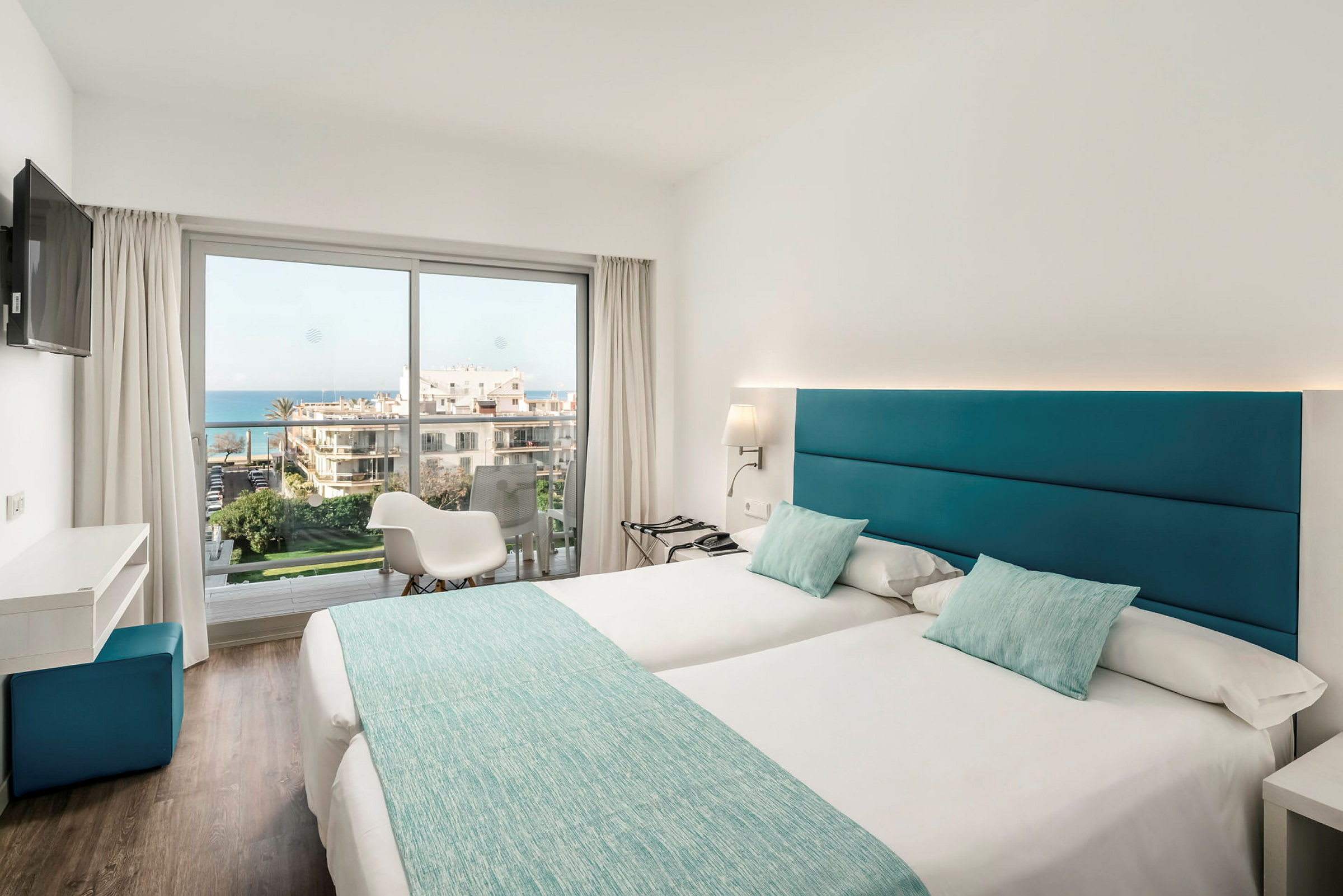 Et lyst hotelværelse med to enkeltsenge, store vinduer og udsigt over havet. (AI-genereret tekst)