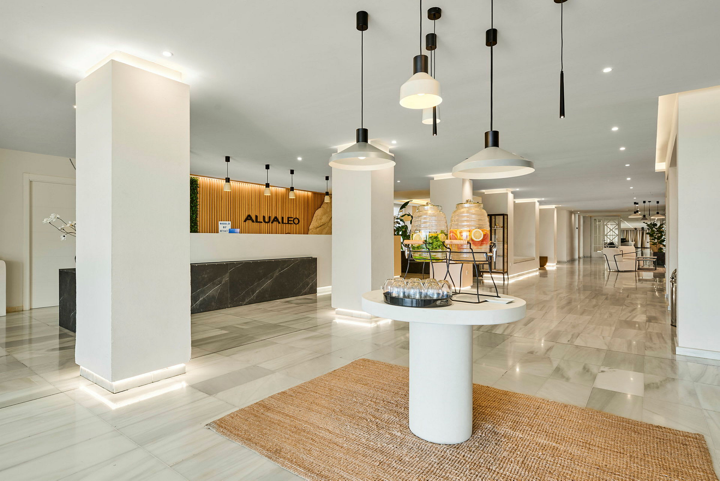 Hotellets lobby med receptionsskranke, en drikkestation og moderne indretning. (AI-genereret tekst)