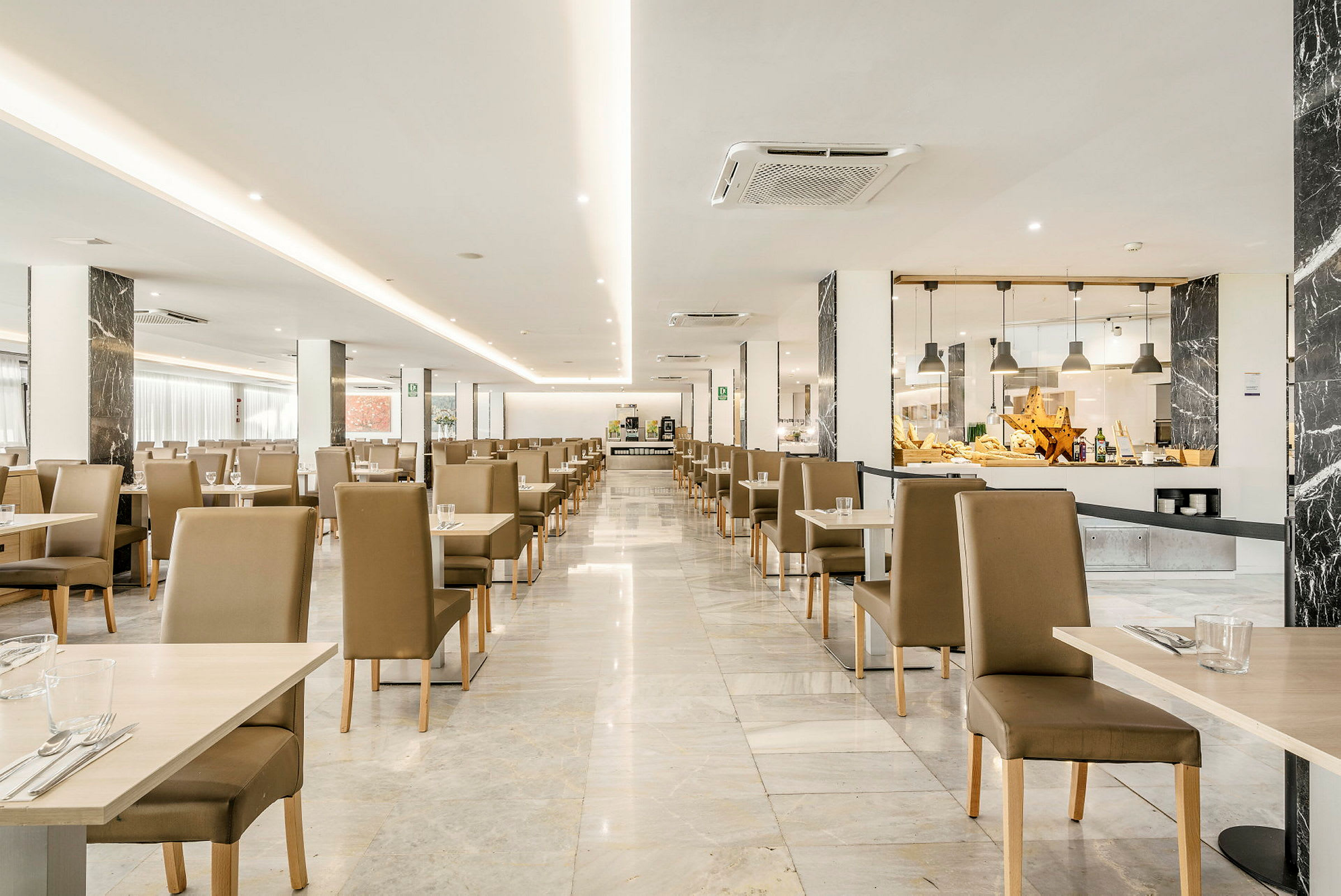 Interiør af en lys restaurant med flere borde og stole opstillet i rækker. (AI-genereret tekst)