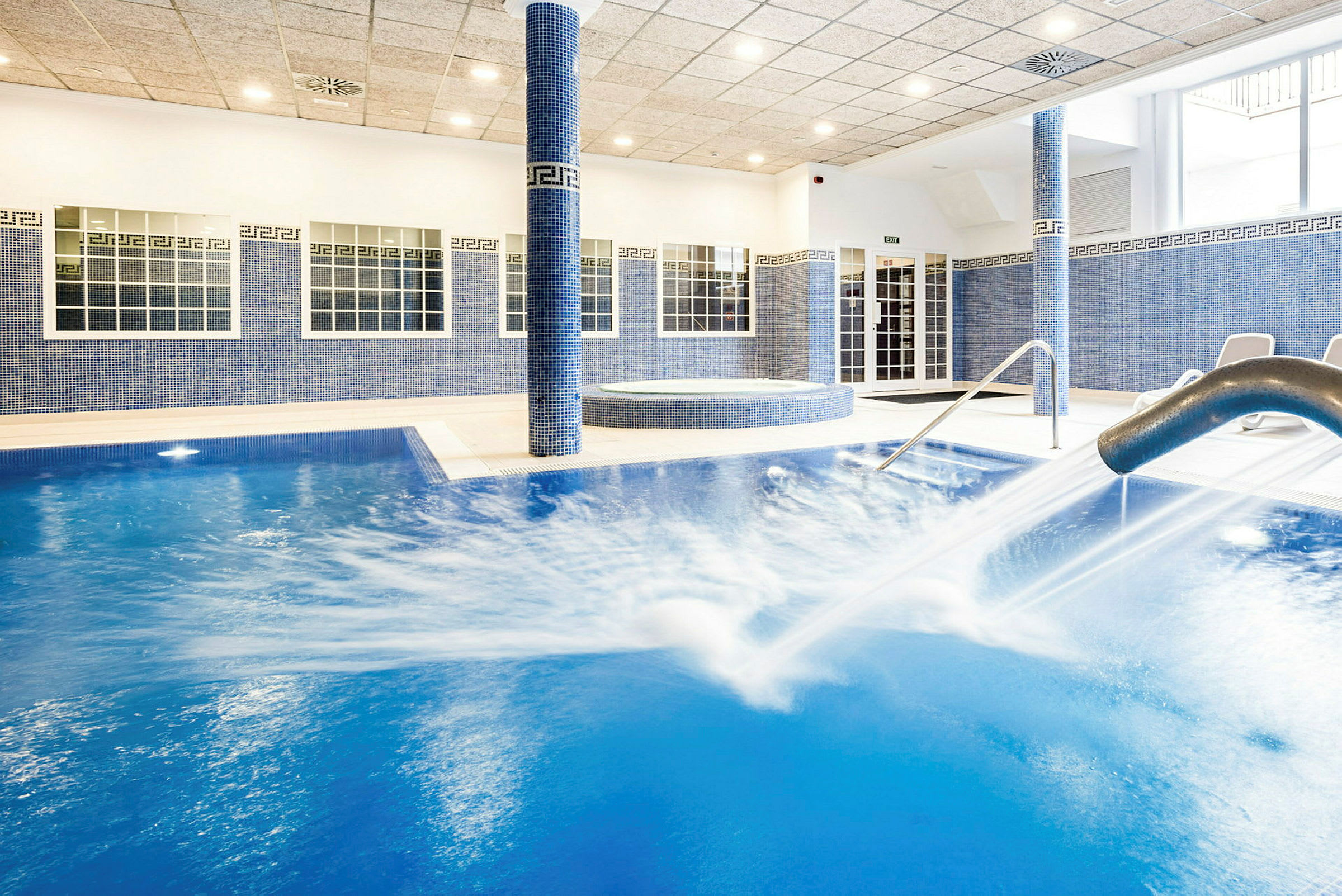 Indendørs swimmingpool med vandstrøm fra en metalstråle. (AI-genereret tekst)