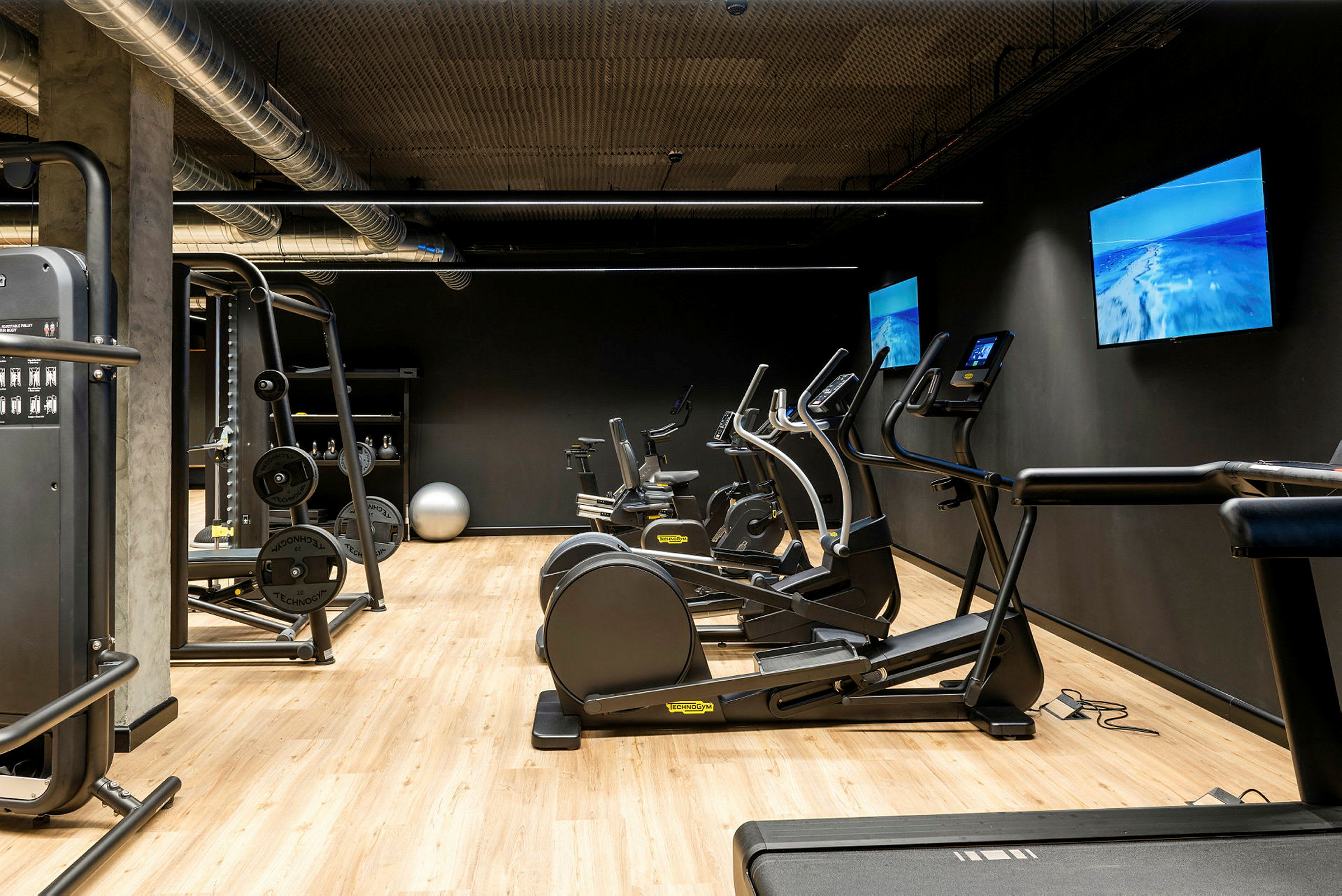Et fitnessrum med træningsudstyr såsom løbebånd, motionscykler og en kabelmaskine. (AI-genereret tekst)