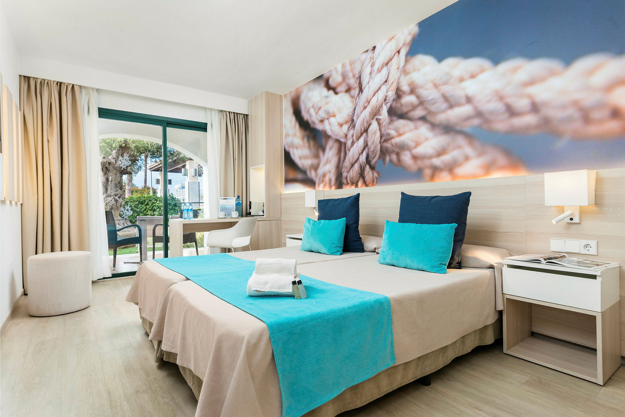 Moderne hotelværelse med to senge, blå detaljer og et billede af reb på væggen. (AI-genereret tekst)