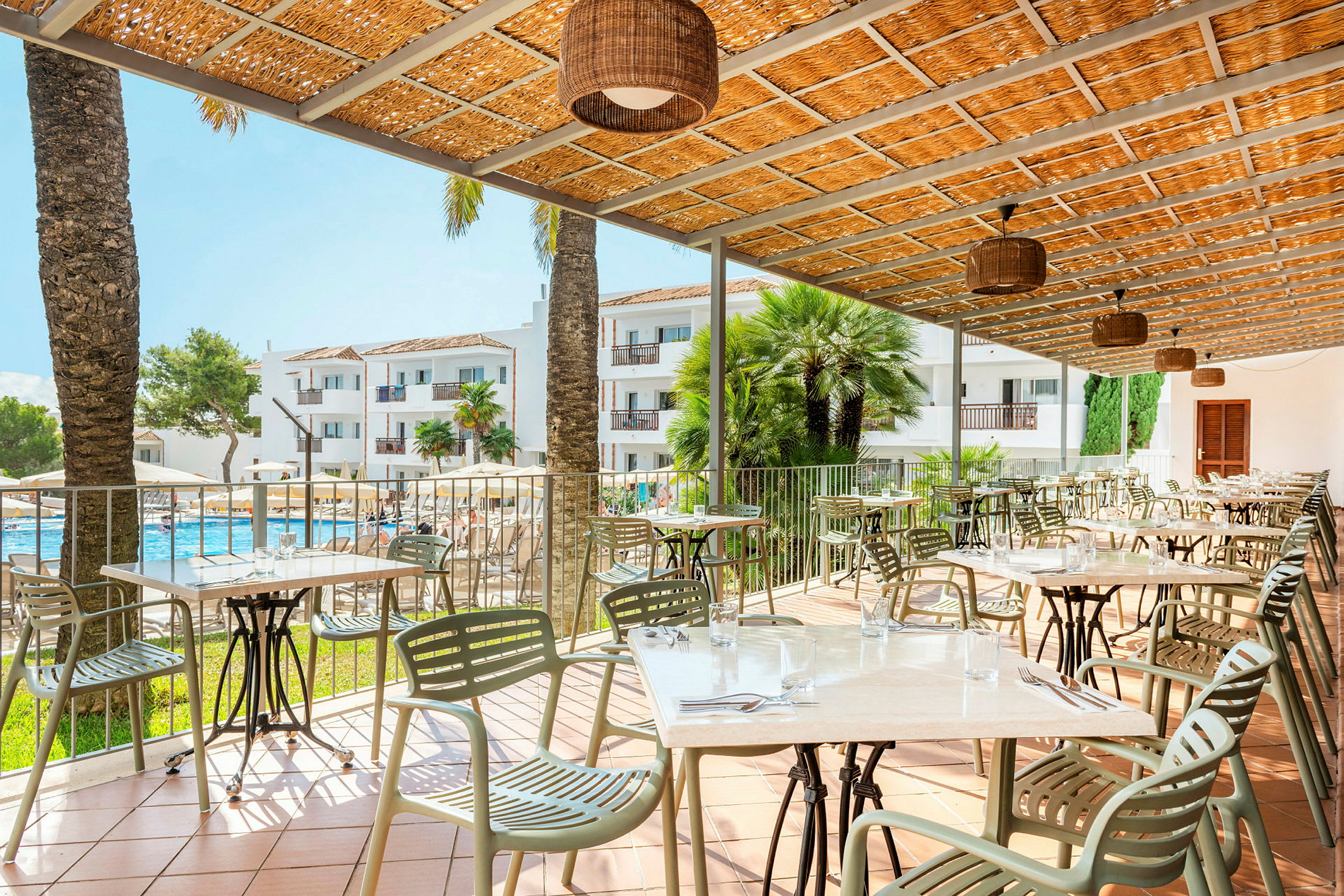 Terrasse med borde og stole, en pool og hotelbygninger i baggrunden. (AI-genereret tekst)