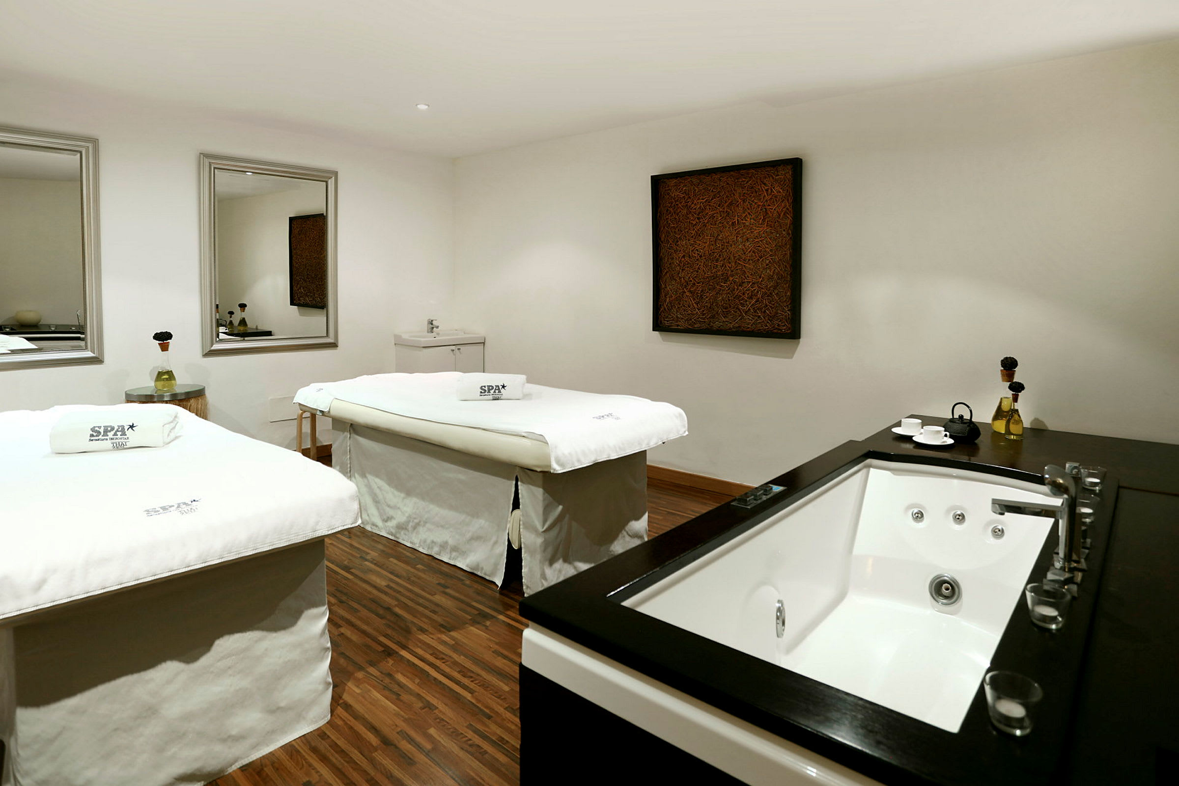Rum med to spa-borde og en jacuzzi på siden, indrettet med spejle og kunst på væggen. (AI-genereret tekst)