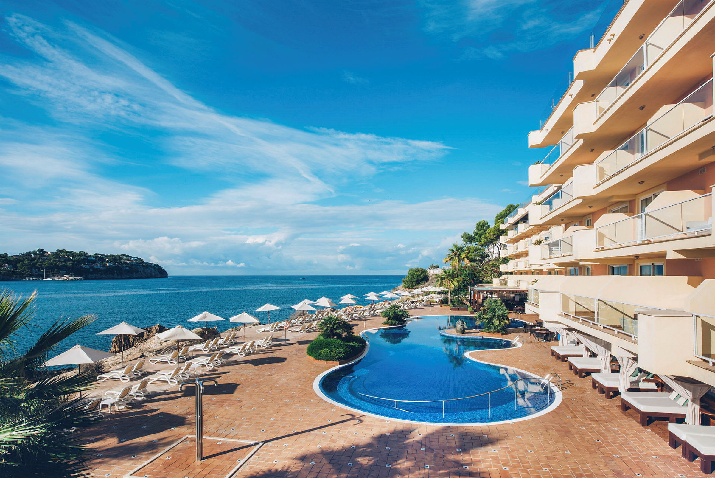 Billede af et hotel ved havet med pool og liggestole. (AI-genereret tekst)