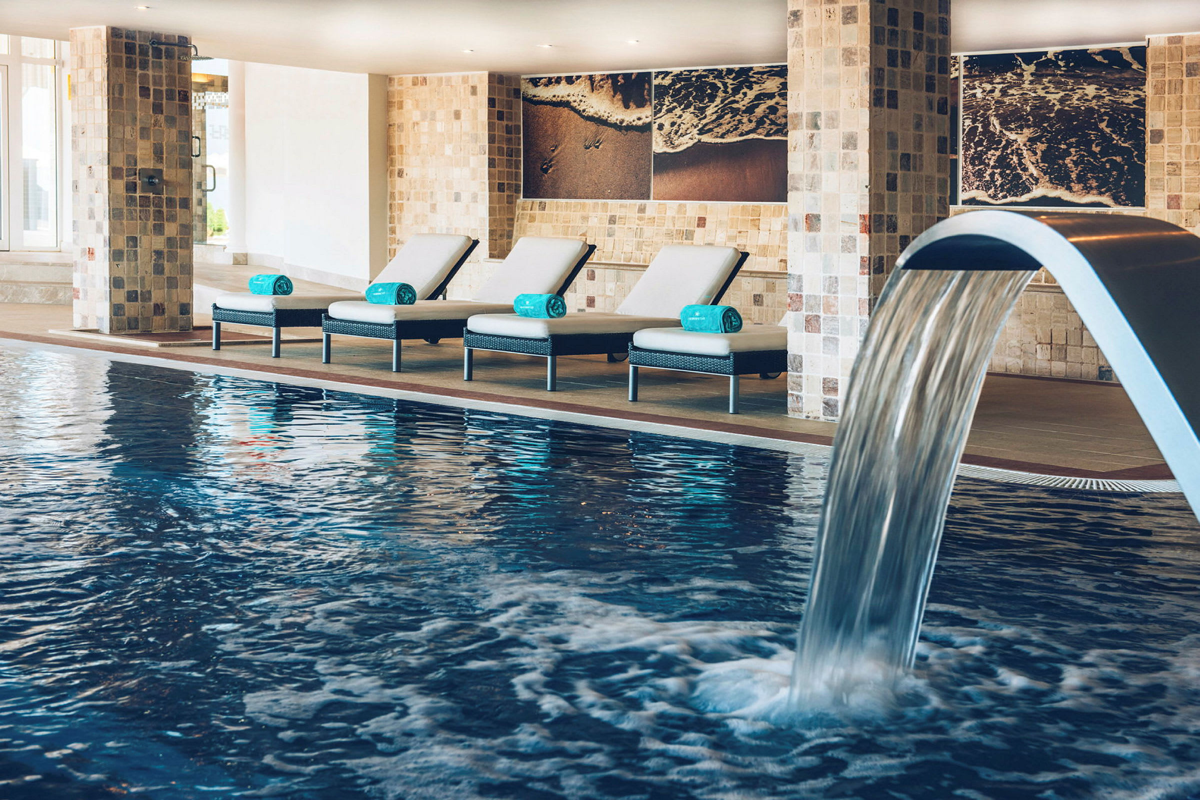 Indendørs swimmingpool med fire liggestole og en vandfontæne. (AI-genereret tekst)