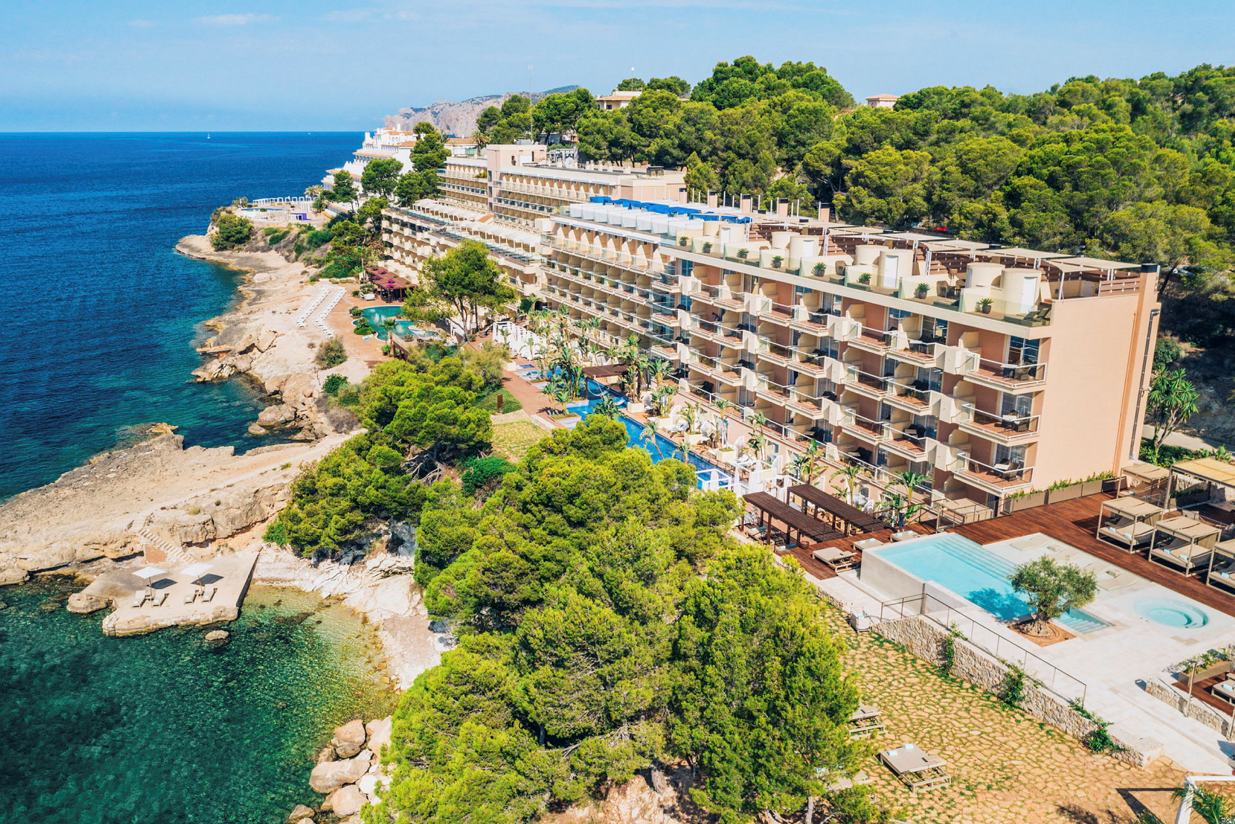 Fleretagers hotel ved kysten med en swimmingpool foran og omkringliggende beplantning. (AI-genereret tekst)