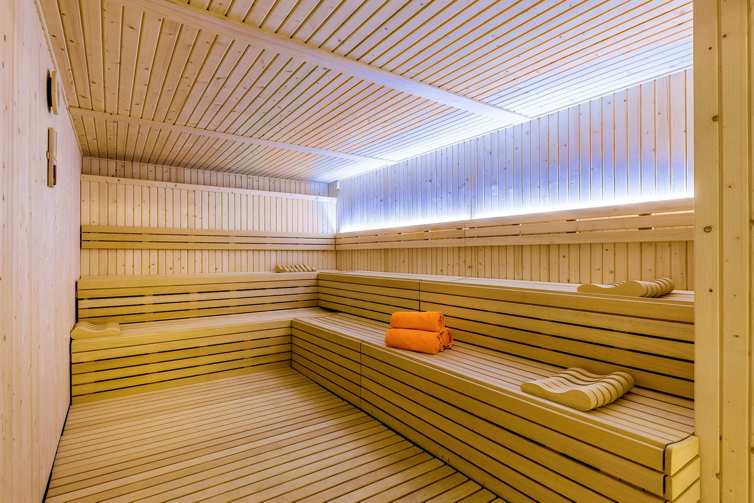 En træbeklædt sauna med bænke og orange håndklæder. (AI-genereret tekst)