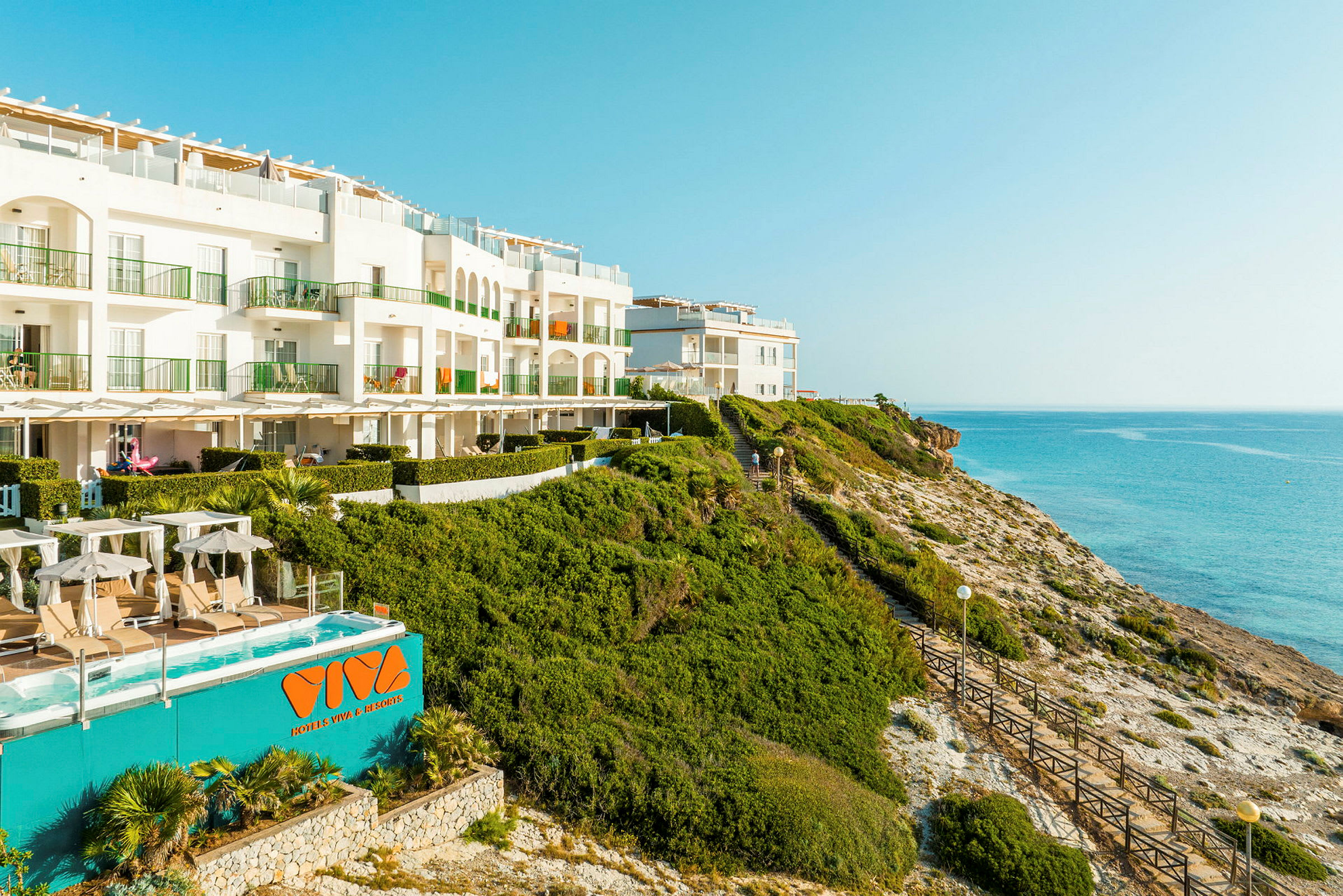 Et hotel beliggende på en klippe ved havet med pool og liggestole. (AI-genereret tekst)