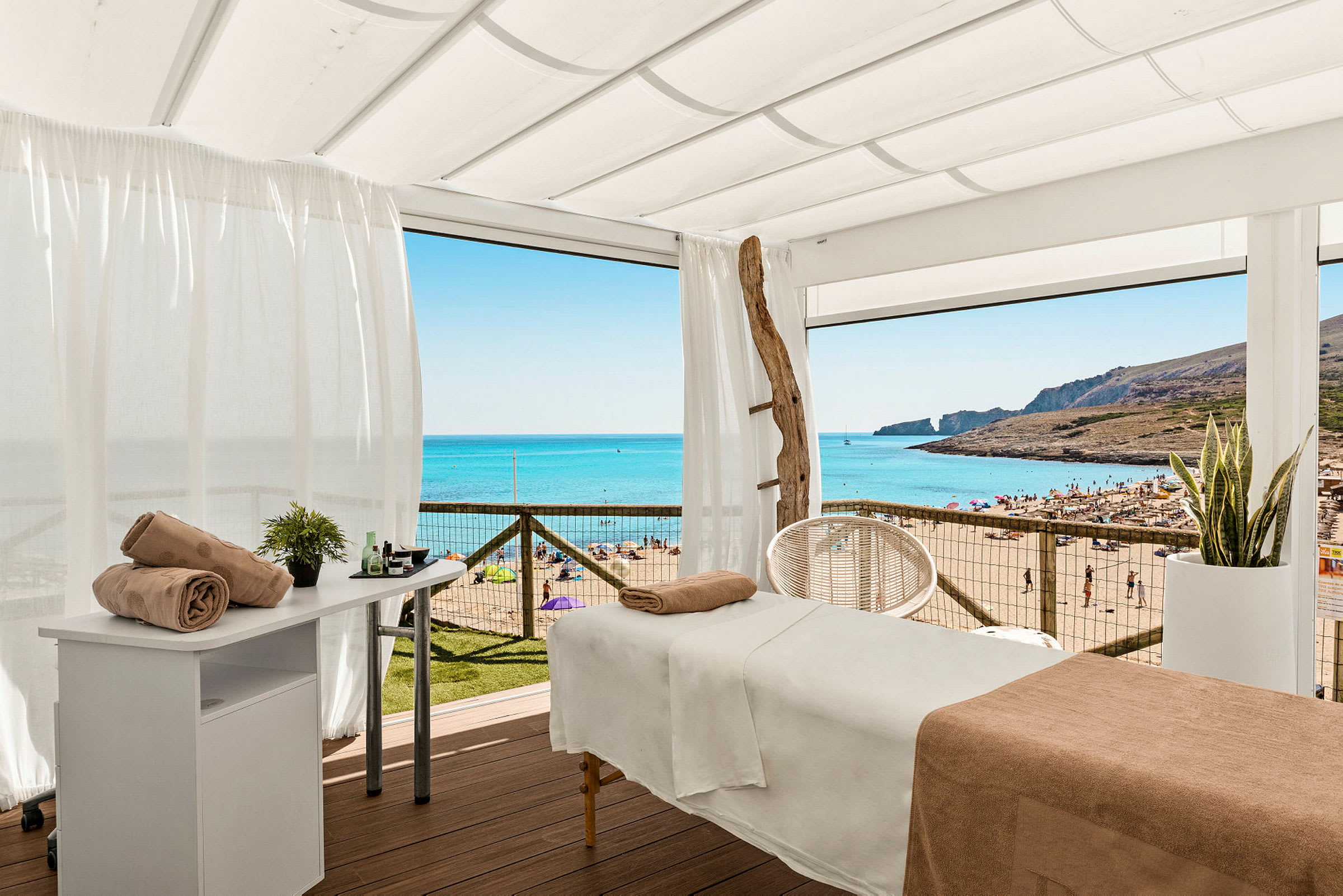Massagebord under en hvid skærm med udsigt over en solrig strand. (AI-genereret tekst)