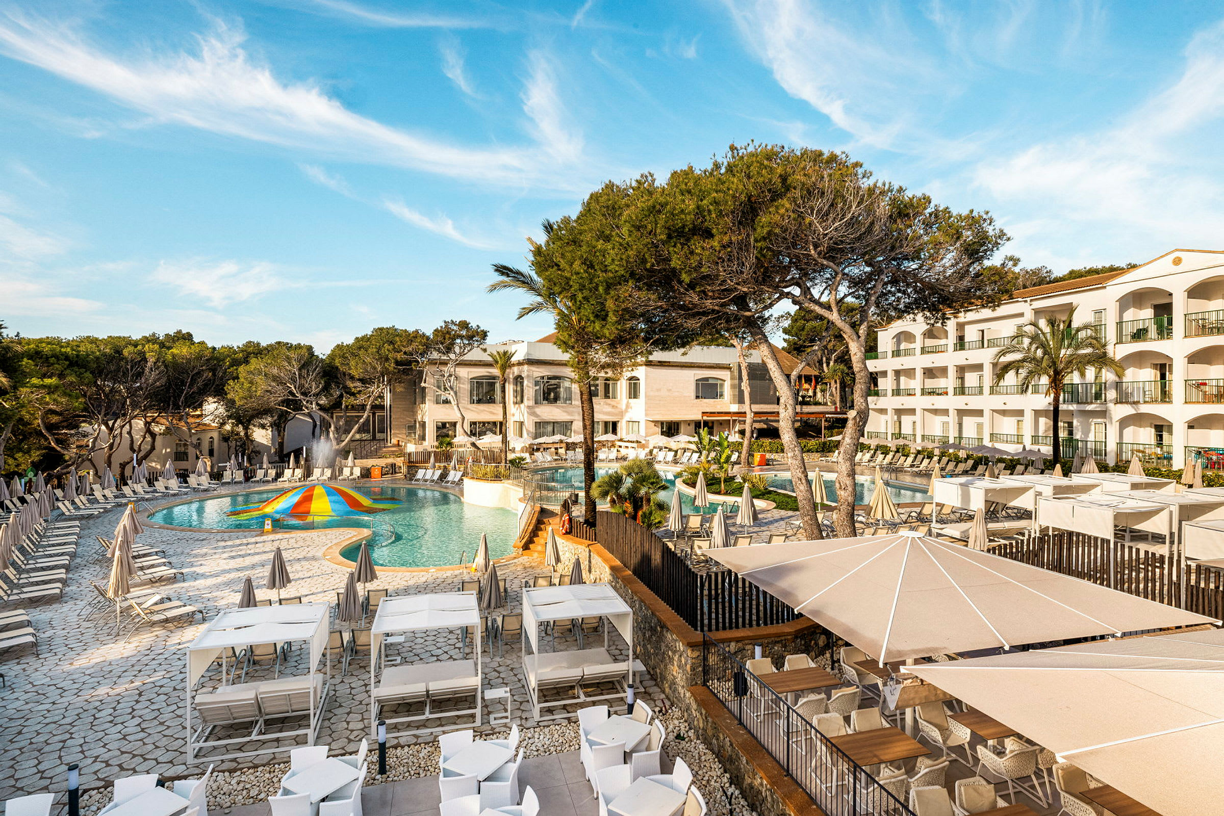 Billede af et hotelområde med pool, solsenge og grønne områder. (AI-genereret tekst)