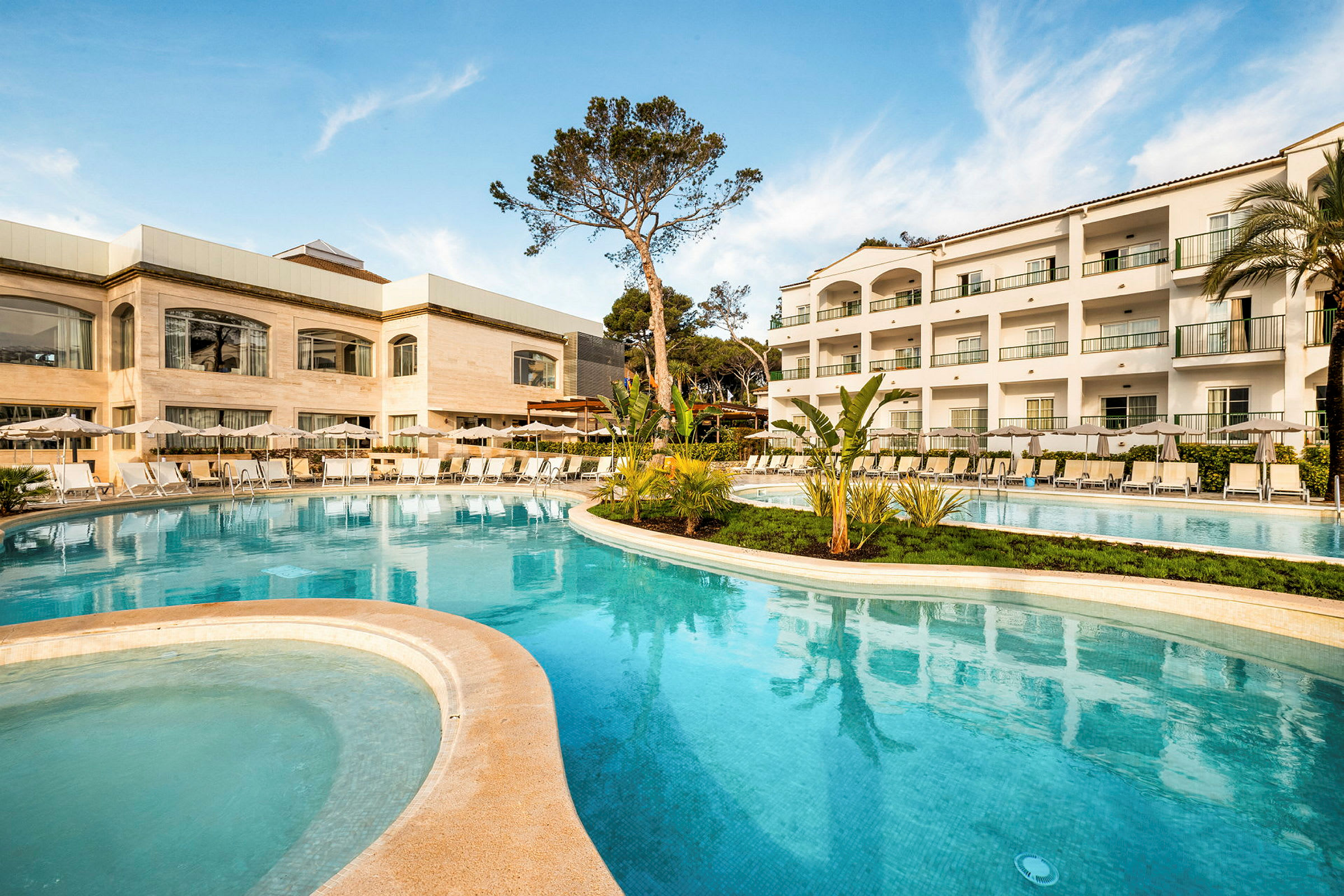 Billede af et hotelområde med swimmingpool, liggestole og en bygning med flere etager. (AI-genereret tekst)