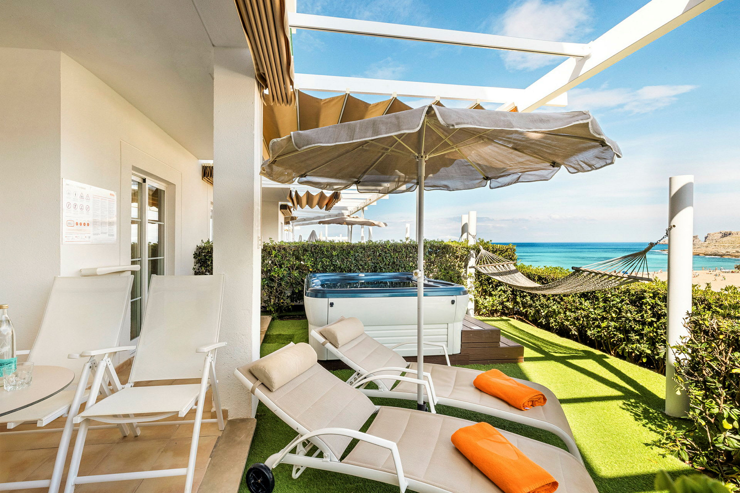 Terrasse med liggestole, parasol, jacuzzi og hængekøje samt udsigt over havet. (AI-genereret tekst)