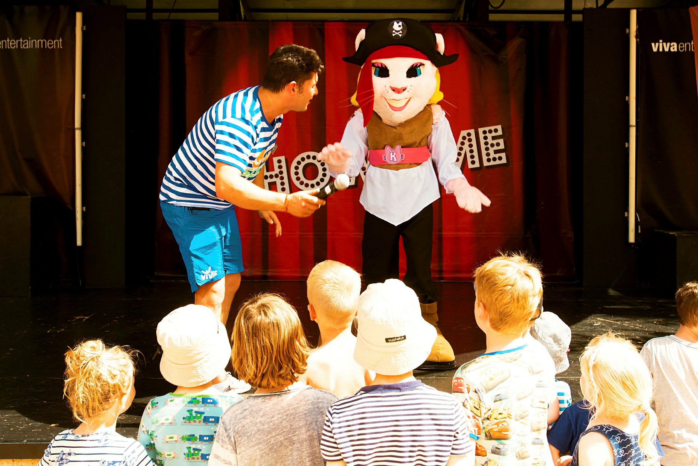 Sceneshow med personer i kostume og børnepublikum. (AI-genereret tekst)
