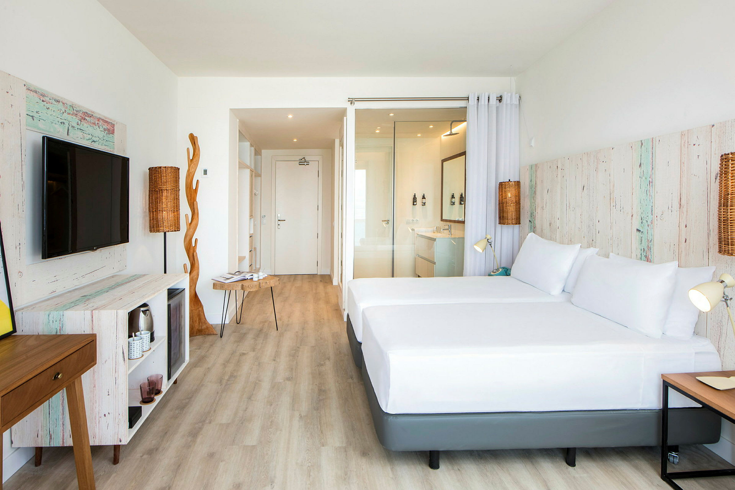Et lyst hotelværelse med trådetailler og moderne møbler. Værelset har en stor seng, et tv og en åben planløsning. (AI-genereret tekst)