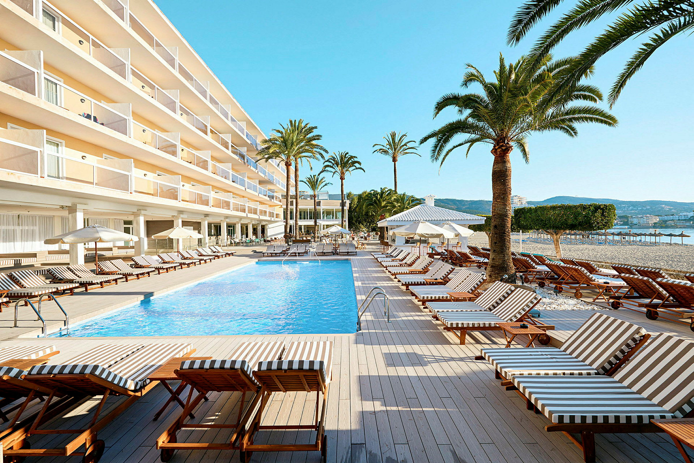 Billede af et hotelområde med en udendørs pool, liggestole og palmer. (AI-genereret tekst)