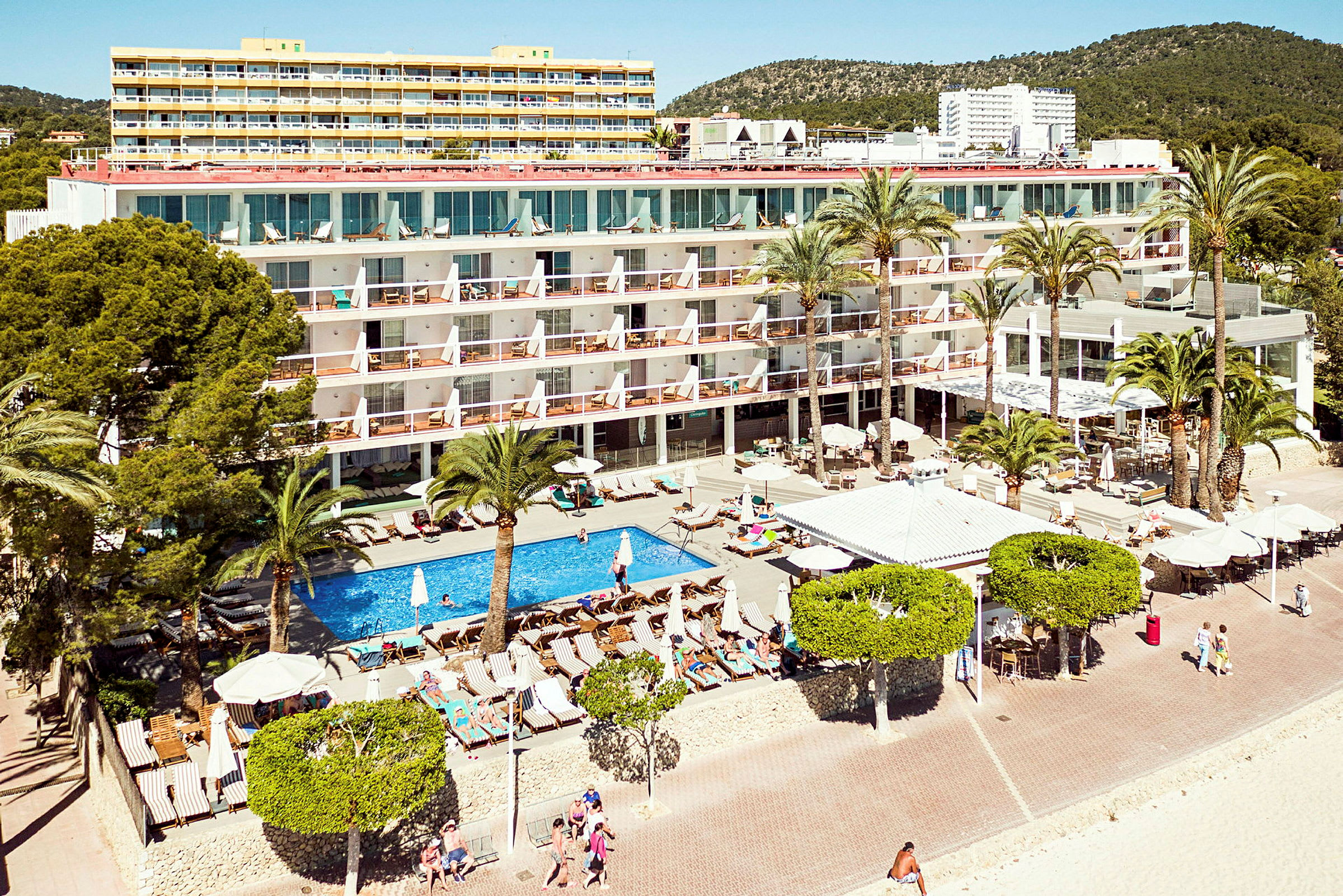Et hotel ved stranden med pool og liggestole omgivet af palmer. (AI-genereret tekst)