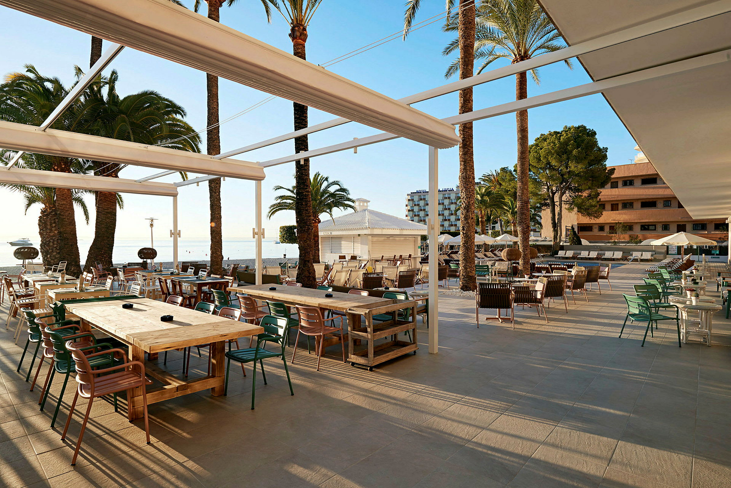 Udendørs terrasse med borde og stole, omgivet af palmer, ved havet. (AI-genereret tekst)
