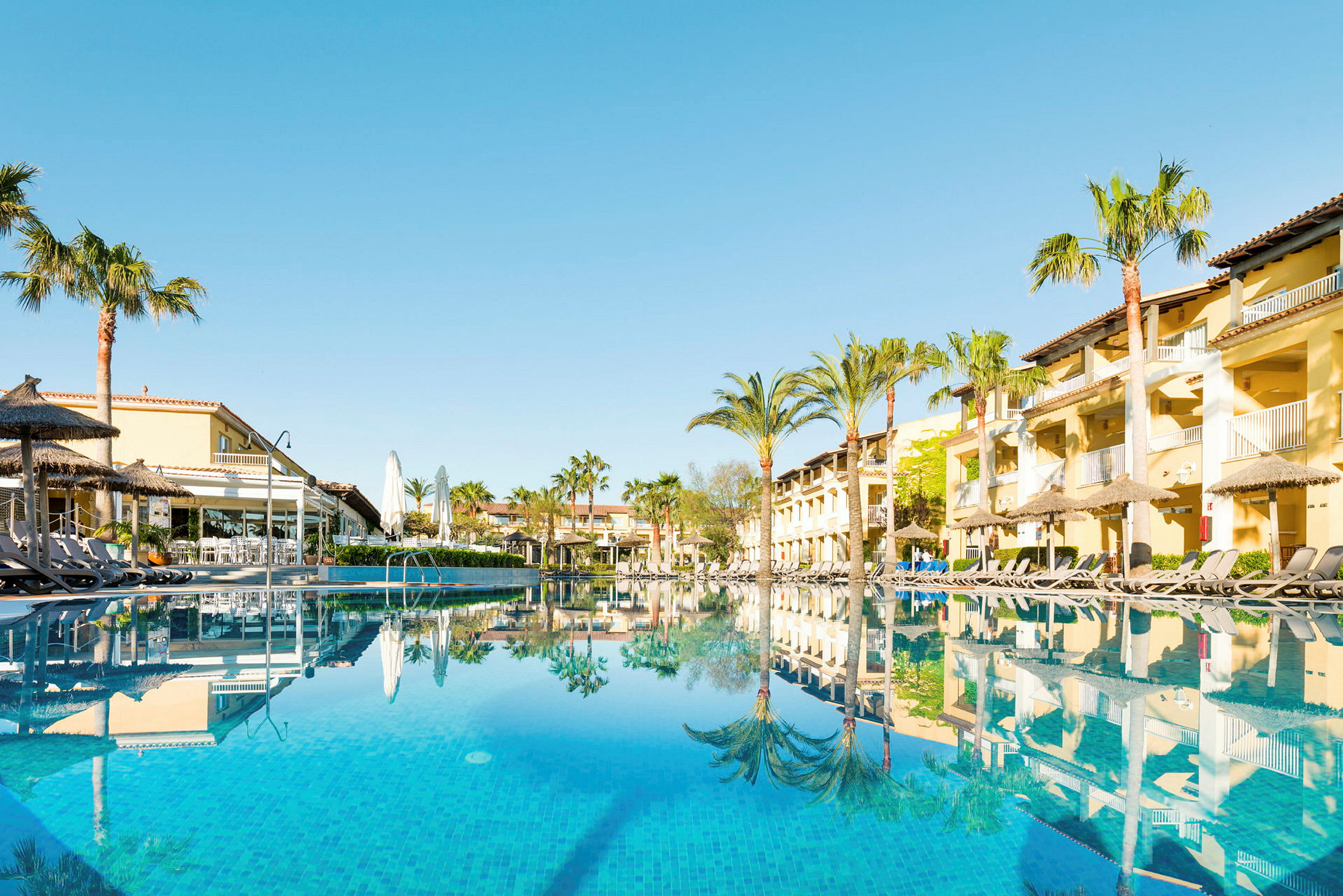 Hotelbygninger og swimmingpool med liggestole ved poolkanten. (AI-genereret tekst)