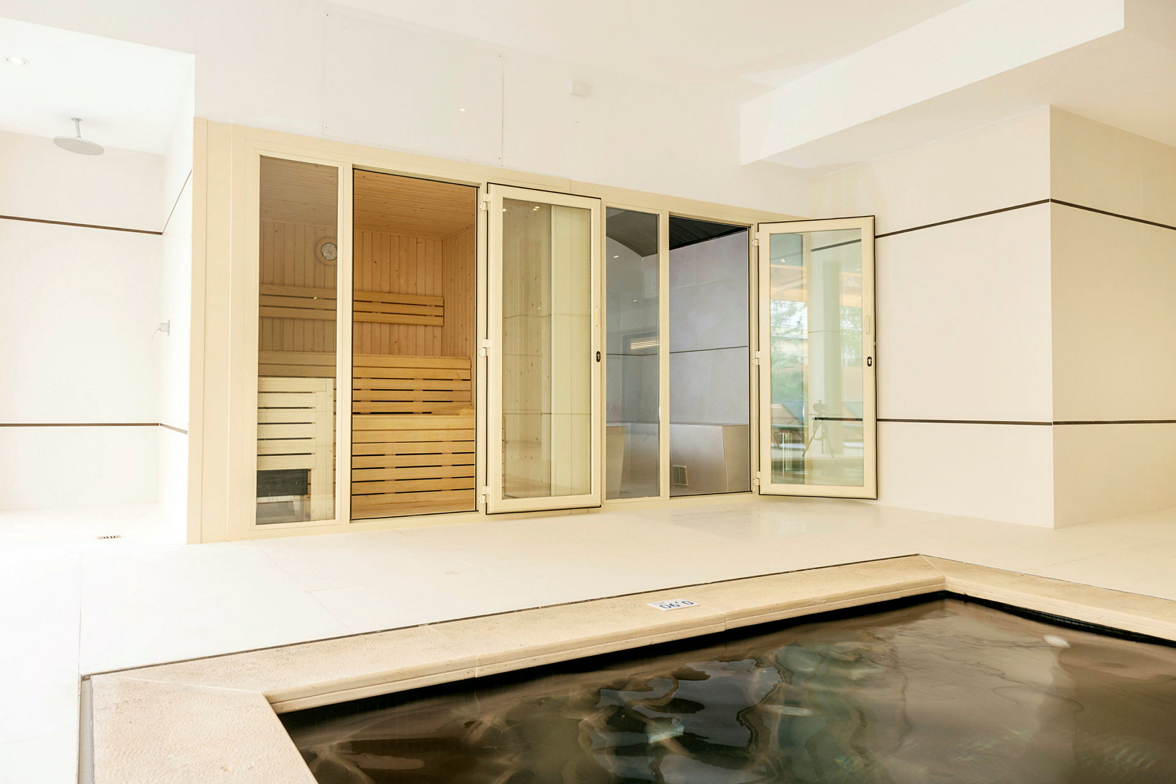 Et indendørsområde med en sauna med glasdøre og en lille pool i forgrunden. (AI-genereret tekst)