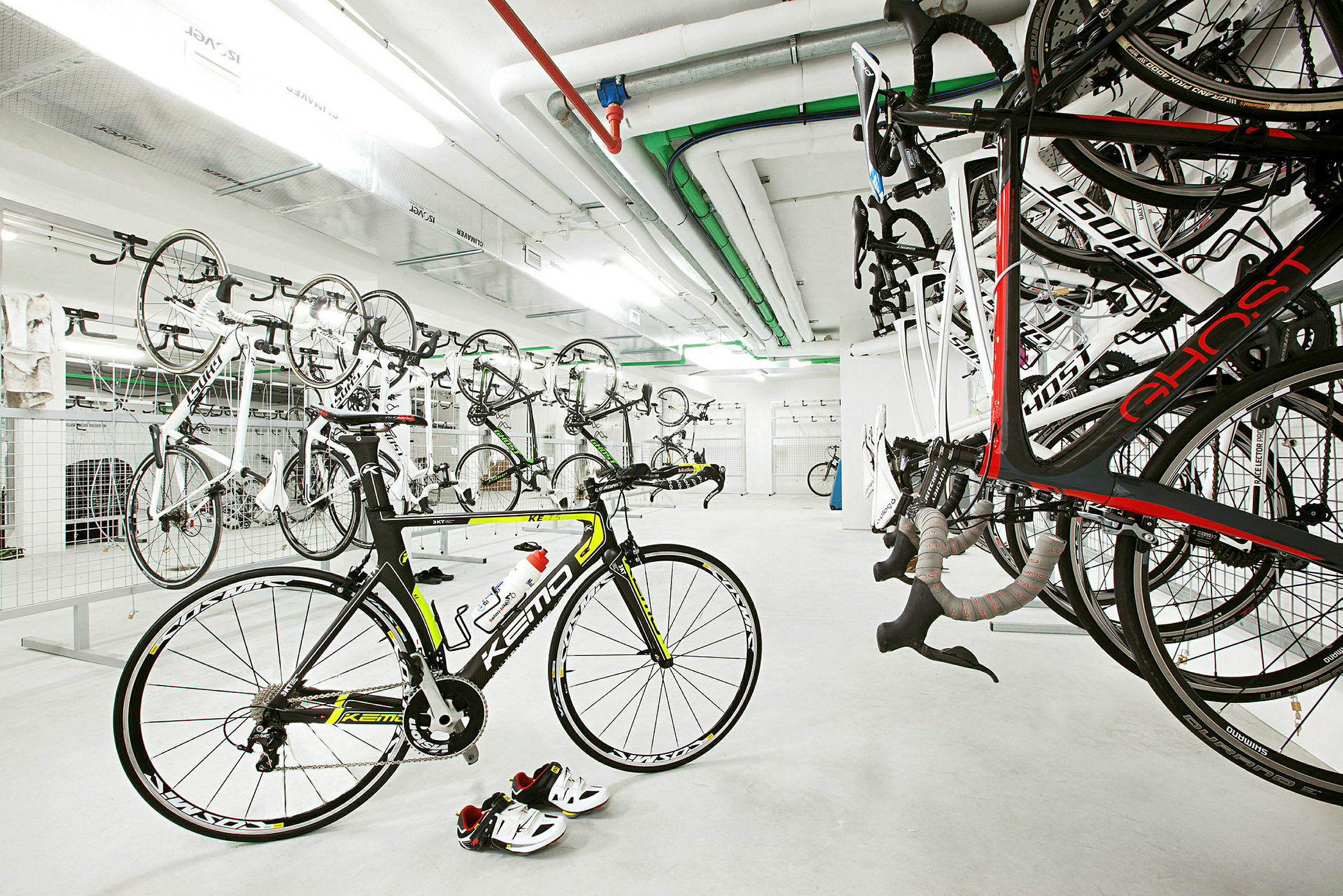 Et cykelrum med flere cykler hængt op på væggen og en cykel stående på gulvet. (AI-genereret tekst)