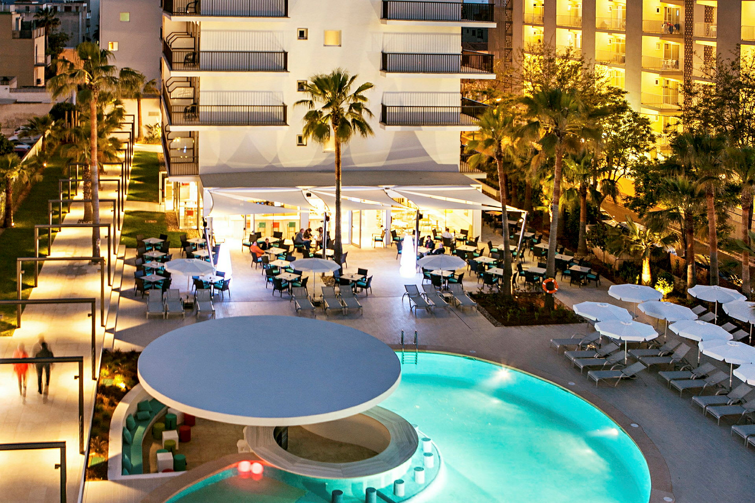 Udendørs hotelområde med pool og udendørs servering om aftenen. (AI-genereret tekst)