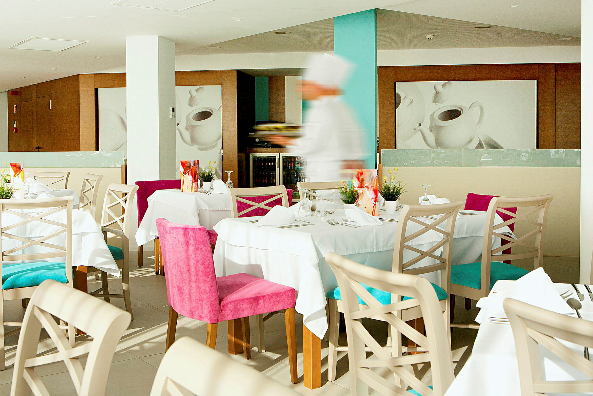 En restaurant med dækkede borde, farverige stole og et sløret billede af en tjener i arbejde. (AI-genereret tekst)