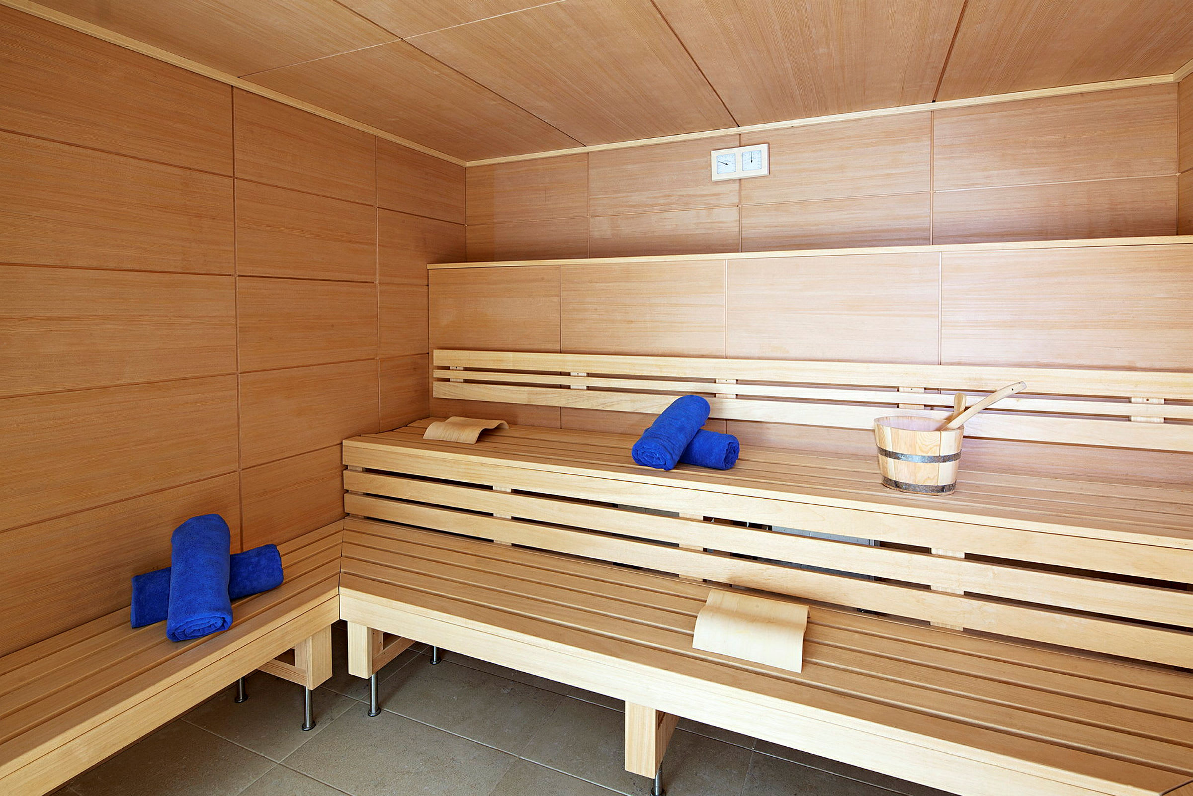 Inde i en sauna, træbænke med blå håndklæder og en saunaspand. (AI-genereret tekst)