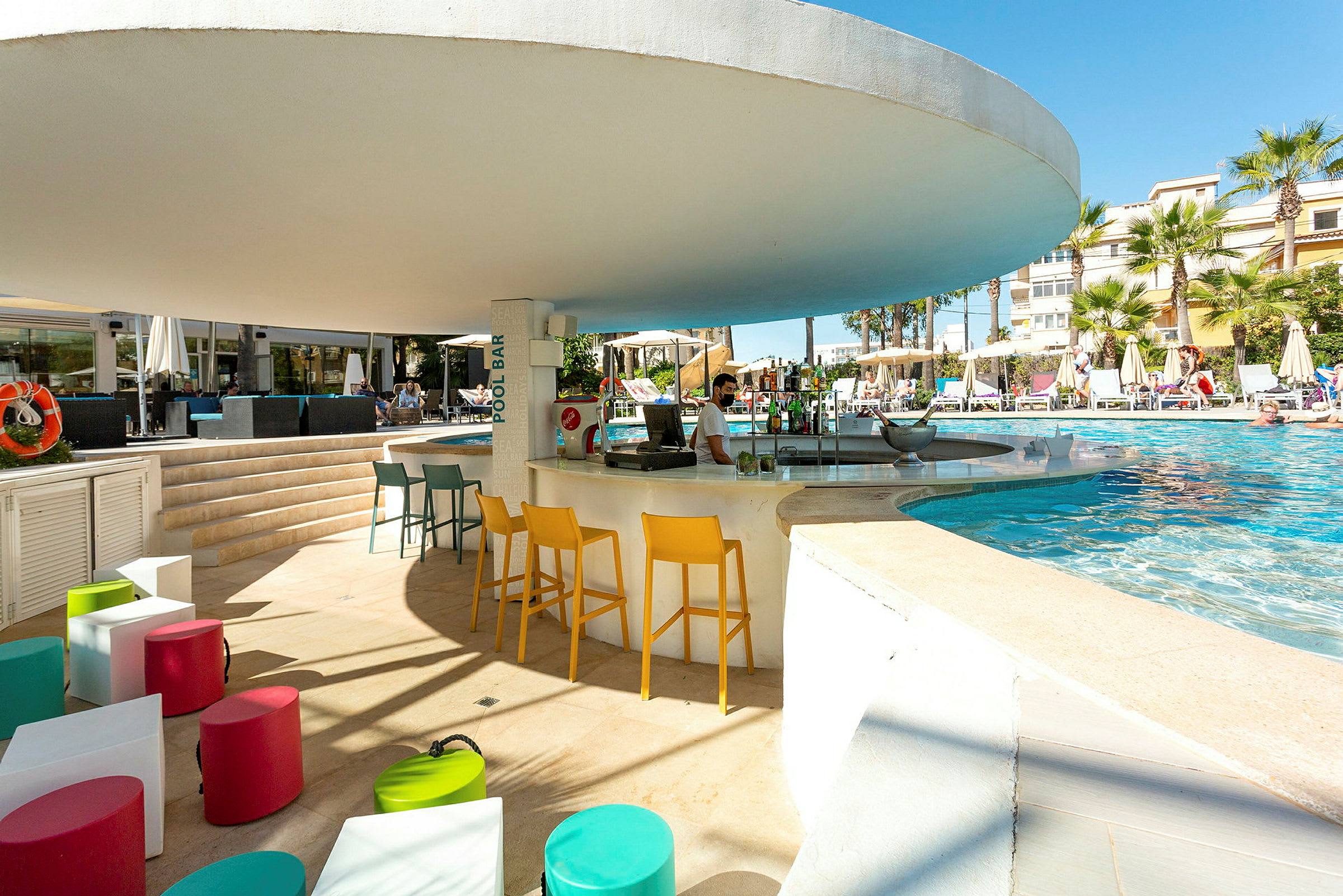 Udendørs poolområde med poolbar og farverige siddepladser. (AI-genereret tekst)
